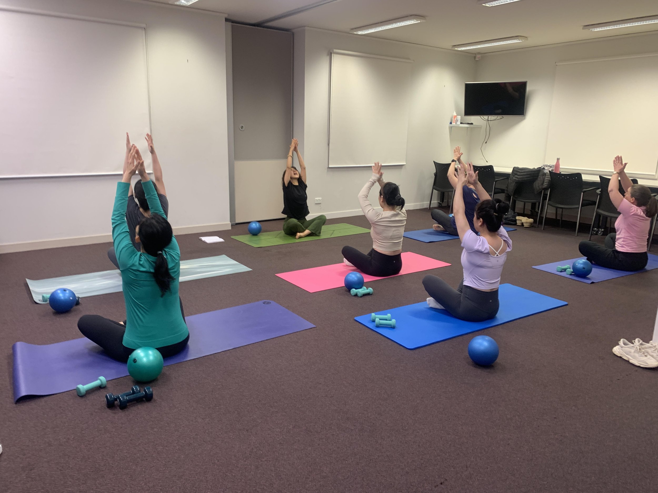 Woman in front of other women seated on yoga mats with arms raised in the air