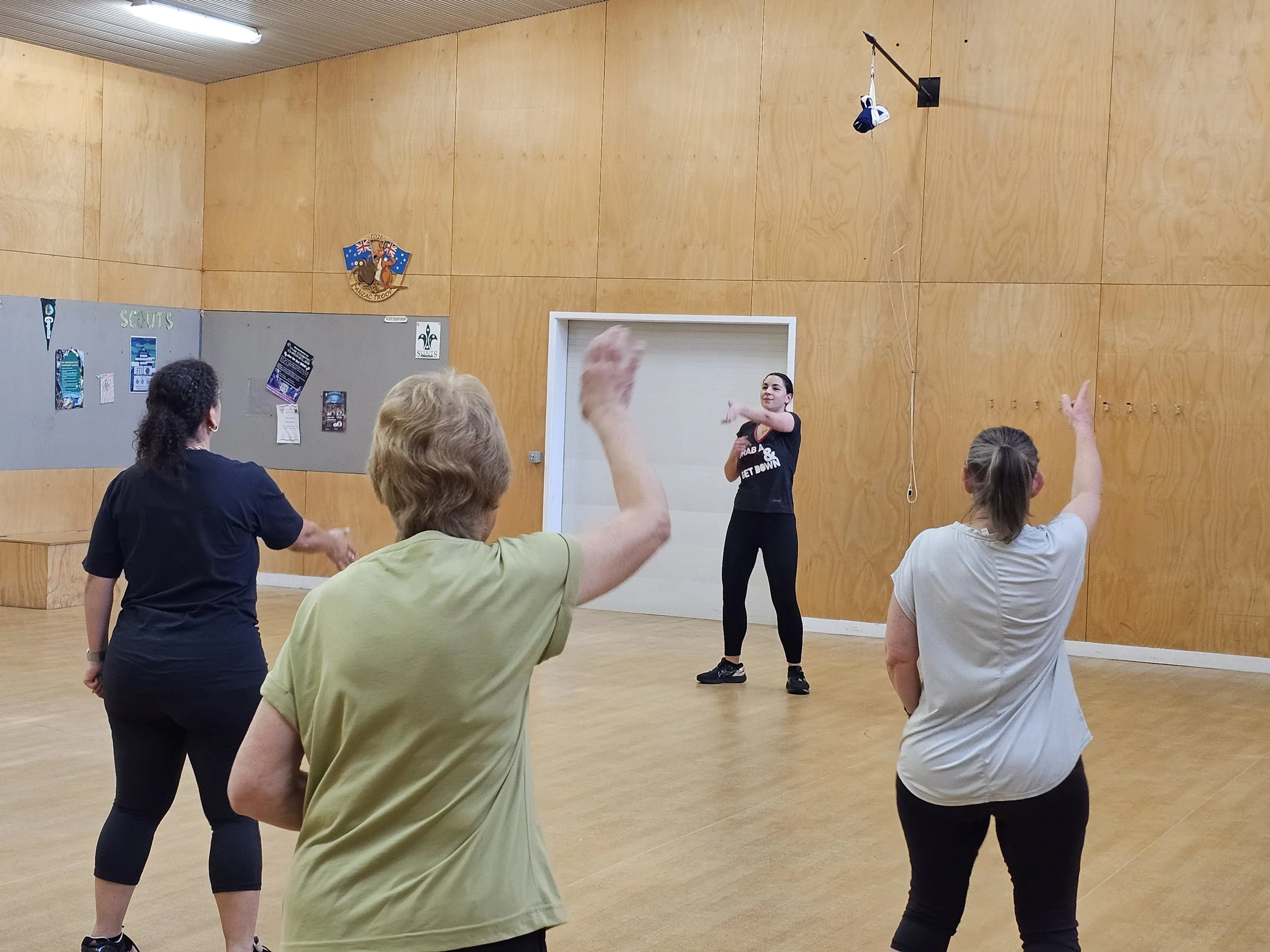 Woman in black standing in front of other women in a hall and showing them how to do different dance moves