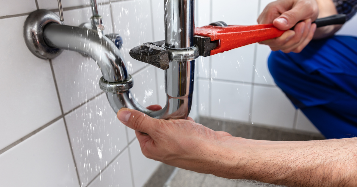 A person fixing a sink pipe with a pipe wrench in a bathroom.