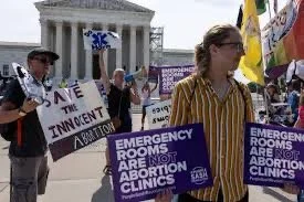 Protesters holding signs about abortion rights and emergency rooms, in front of a significant government building, possibly during a demonstration.