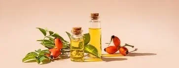 Two small bottles of yellow essential oil, surrounded by green leaves, small orange and red flowers, on a light background.