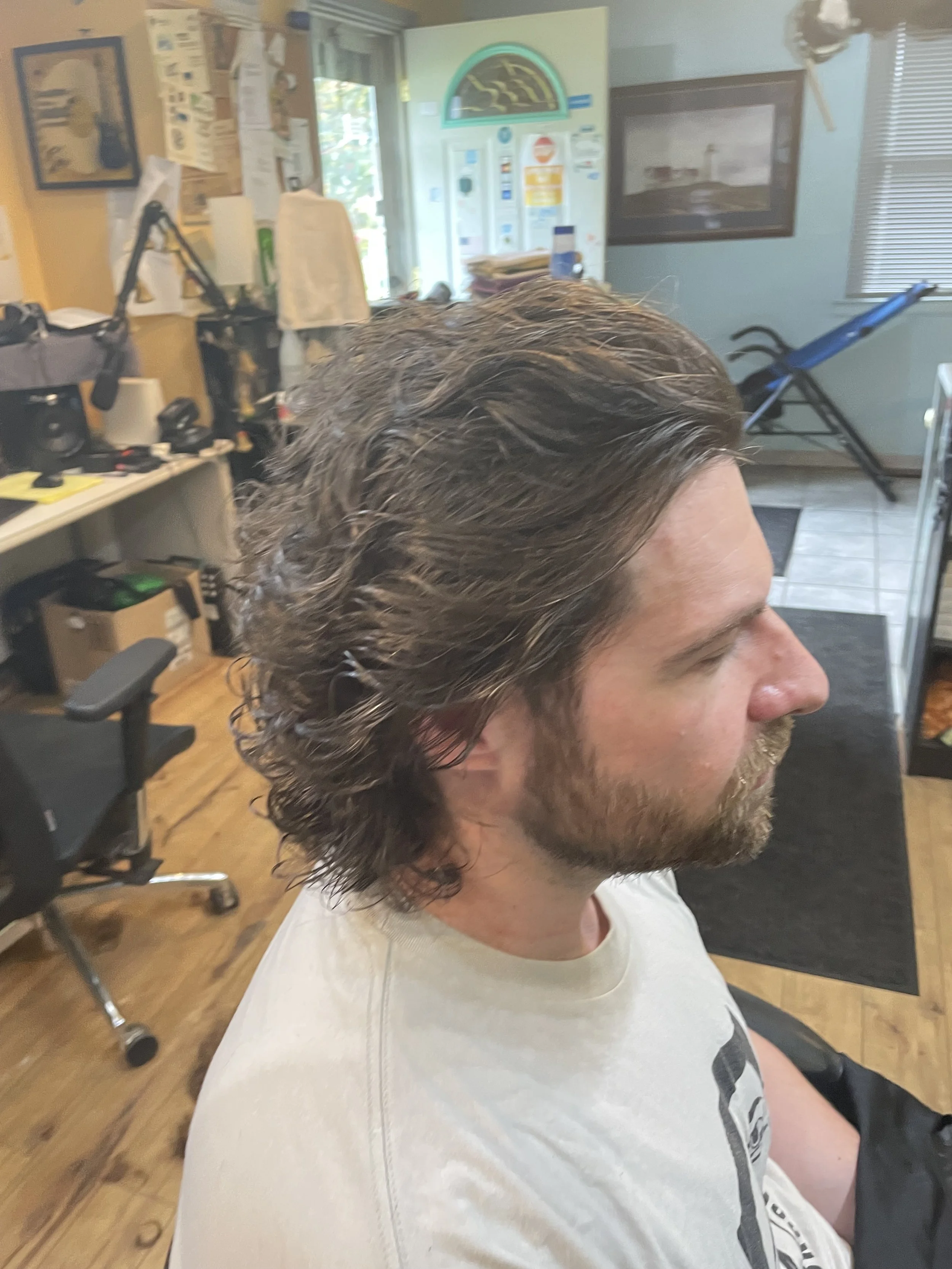 A man with wet, wavy brown hair sitting in a salon or barber shop chair.