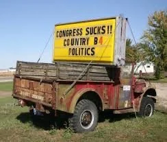 Old red truck with a large yellow political billboard on it that reads 'CONGRESS SUCKS!!' and 'COUNTRY B4 POLITICS'.