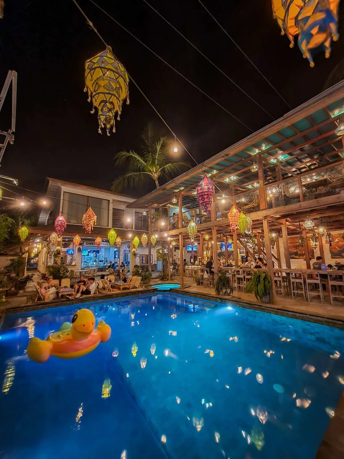 Romantic evening dining atmosphere at Pesona Lounge Gili Trawangan overlooking the swimming pool with warm lantern lighting and outdoor seating.