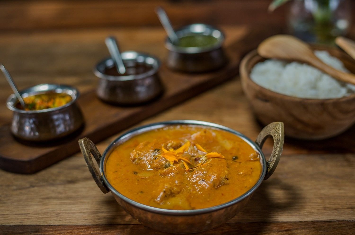 Butter chicken curry served in a traditional metal bowl with rice and side dishes at Pesona Lounge Trawangan.