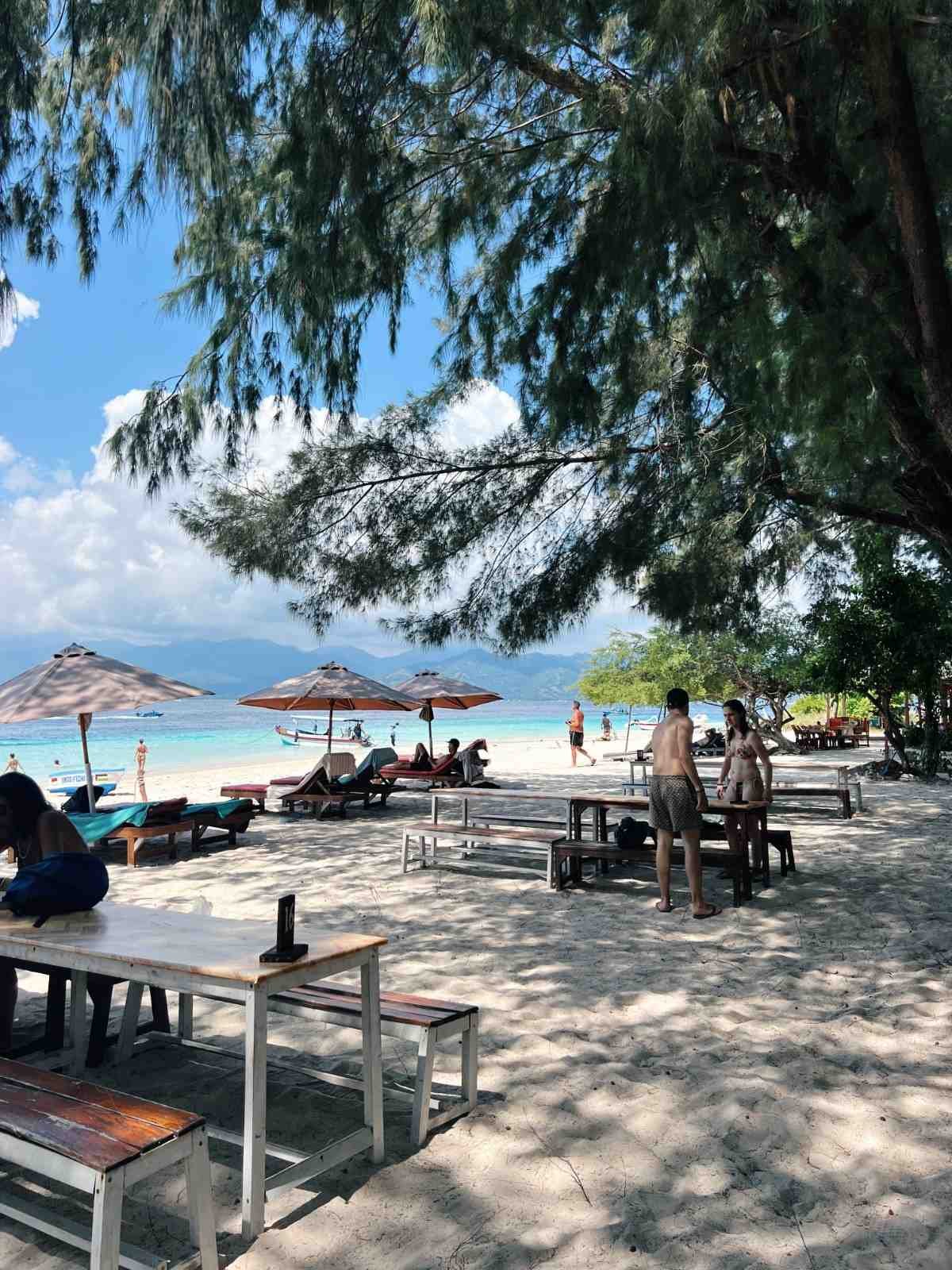 Beachfront dining area at Pesona Lounge Gili Trawangan surrounded by tropical trees and ocean views