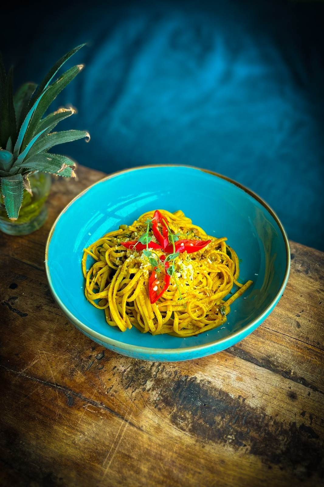 Bombay Garlic Chili Pasta topped with sliced red chillies and herbs in a turquoise bowl at Pesona Lounge Trawangan.