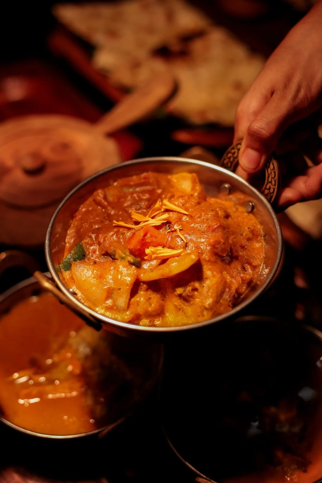 A hand holding a bowl of Chicken Tikka Masala curry, garnished with flower petals at Pesona Lounge Trawangan