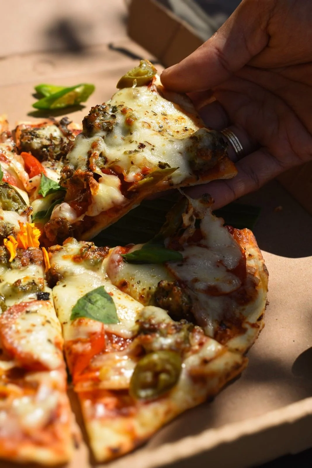 Hand lifting a slice of Meat Feast Naan Pizza topped with cheese and herbs at Pesona Lounge Trawangan.