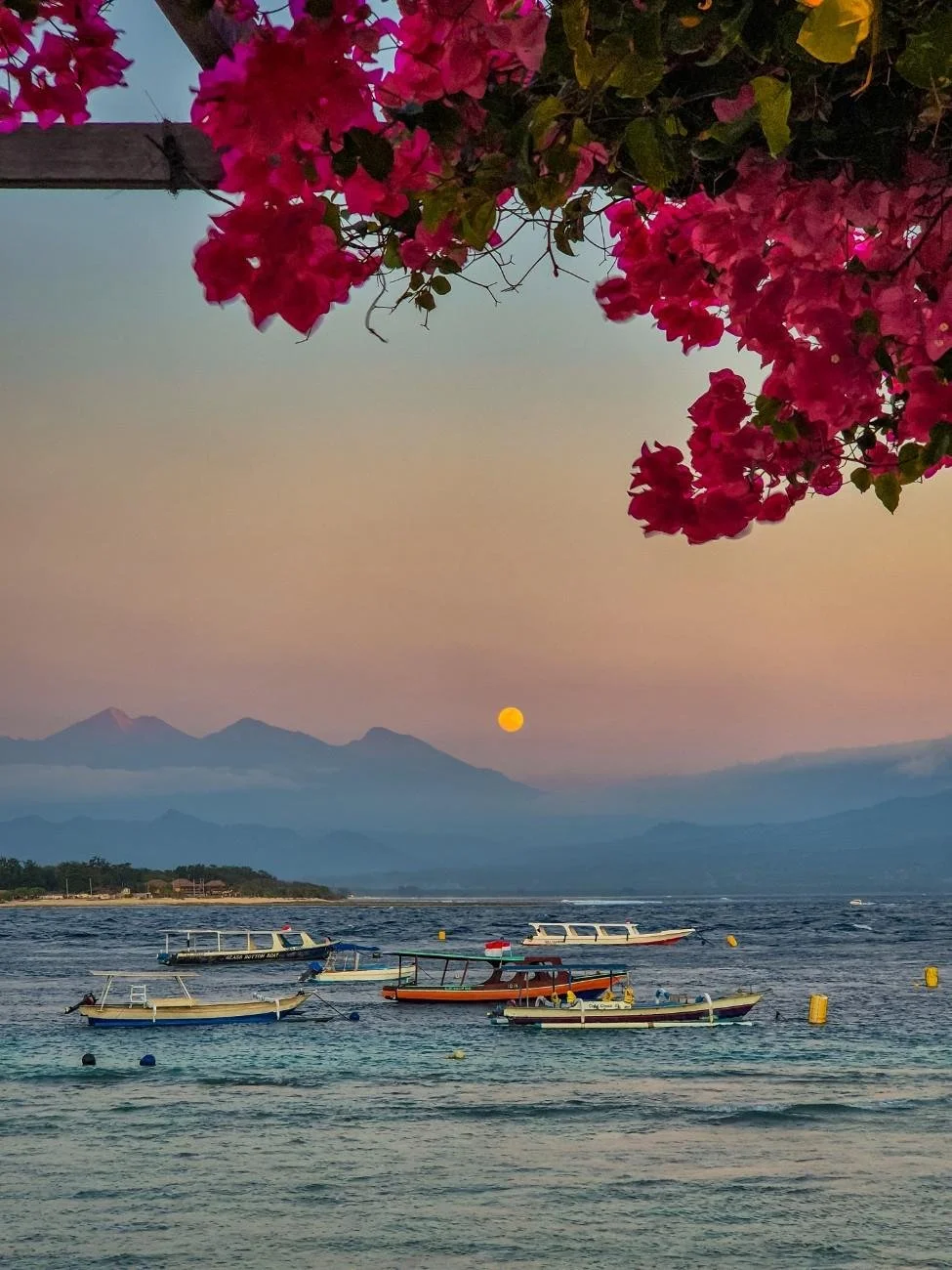 Sunset view over Gili Trawangan with traditional boats anchored offshore and Mount Agung visible in the distance