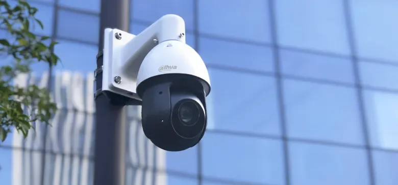Security camera mounted on a pole in front of a glass building.