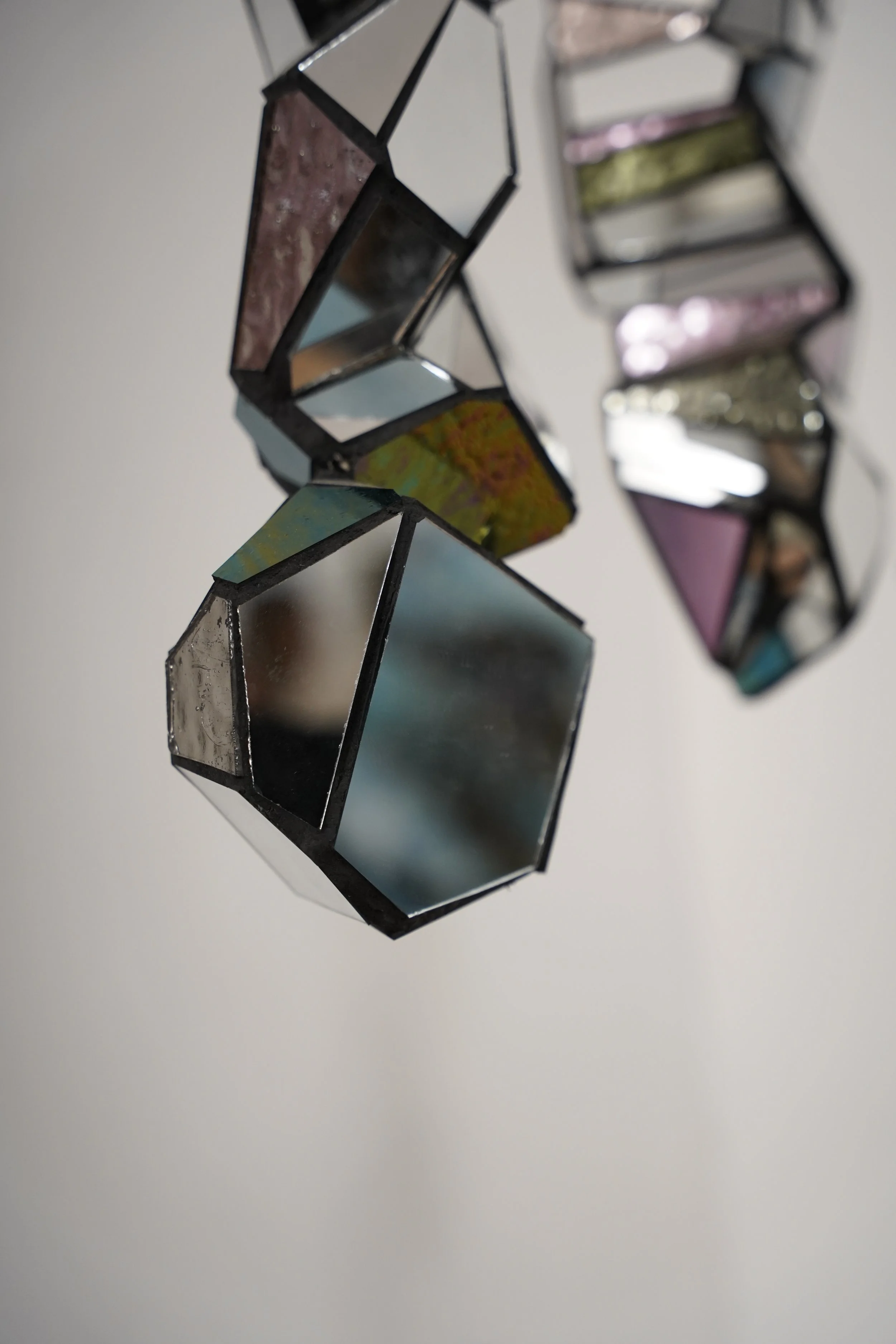 Close-up of a geometric, stained-glass style hanging ornament with various colored glass panels, suspended against a plain white background.