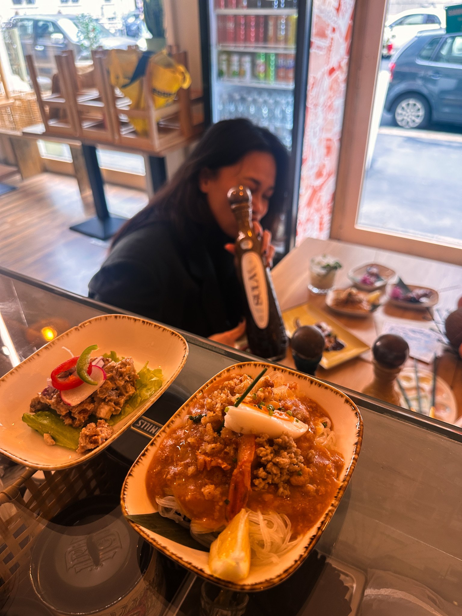 Asian dishes on a table, including noodles with sauce and lettuce wraps, with a bottle of olive oil in the background.