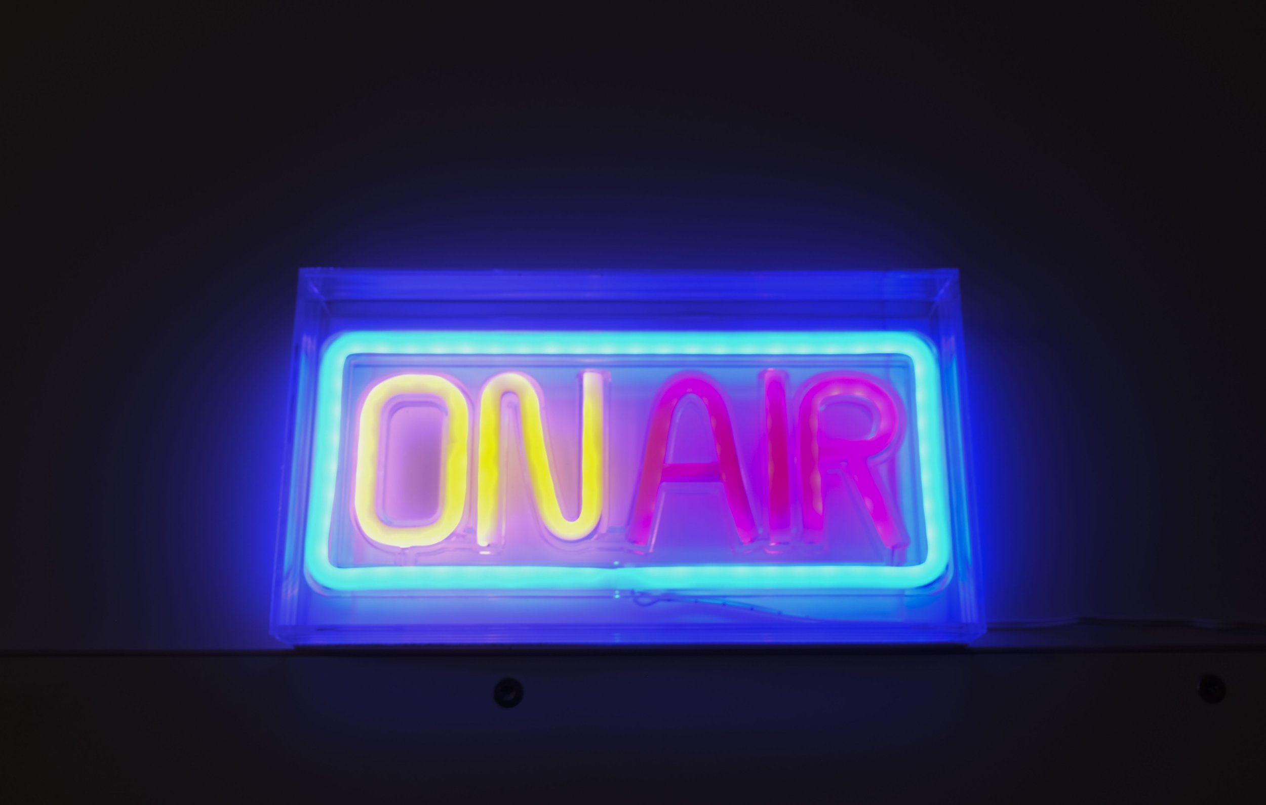 Neon-Schilder mit dem Wort "ON AIR" in leuchtenden Farben, installiert in einem dunklen Raum.