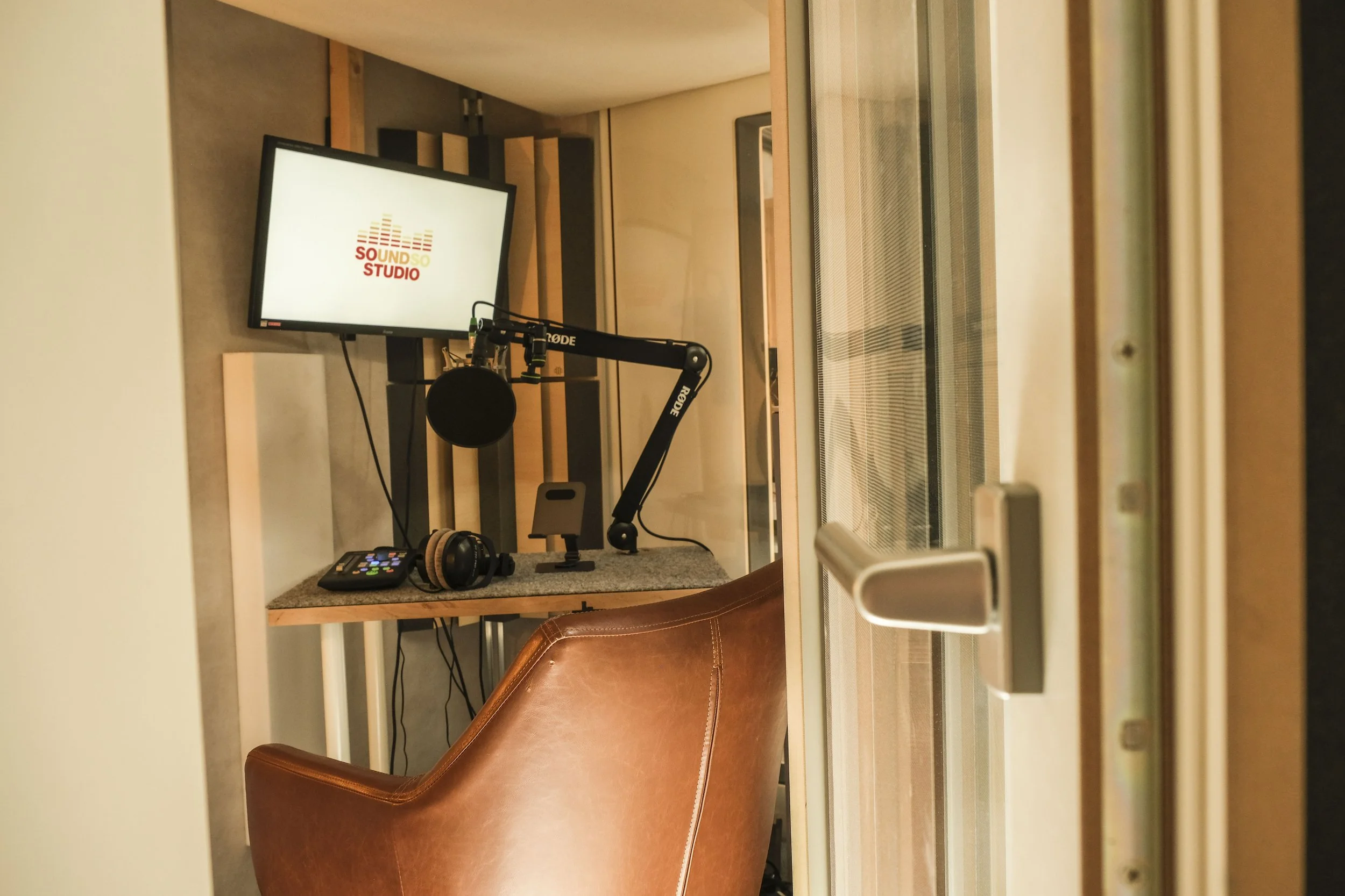 Aufnahme eines Aufnahmestudios mit einem Monitor, einem Mikrofon, Kopfhörern und einem Mischpult. Der Bildschirm zeigt das Logo 'SOUND SO STUDIO'.