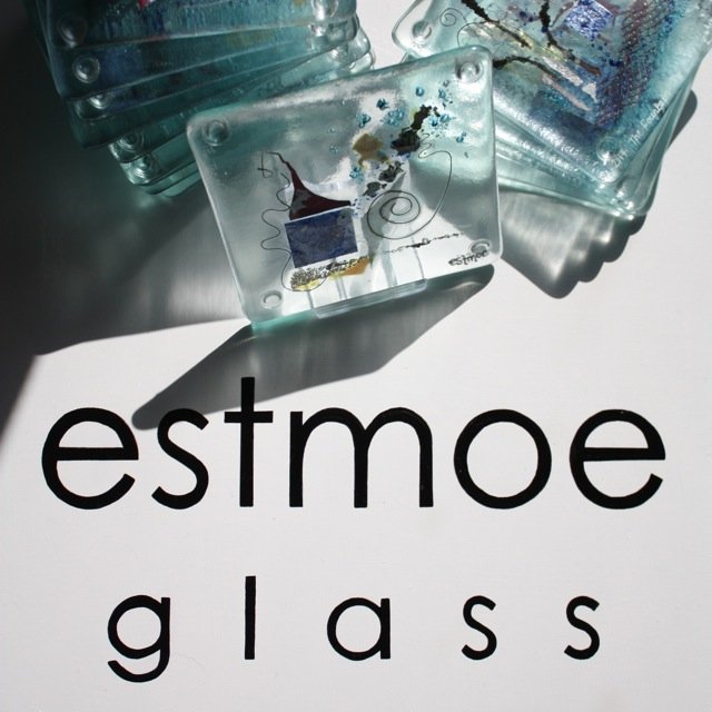 Close-up of decorative glass art pieces with abstract designs, placed on a white surface with the words 'estmpe glass' printed underneath.