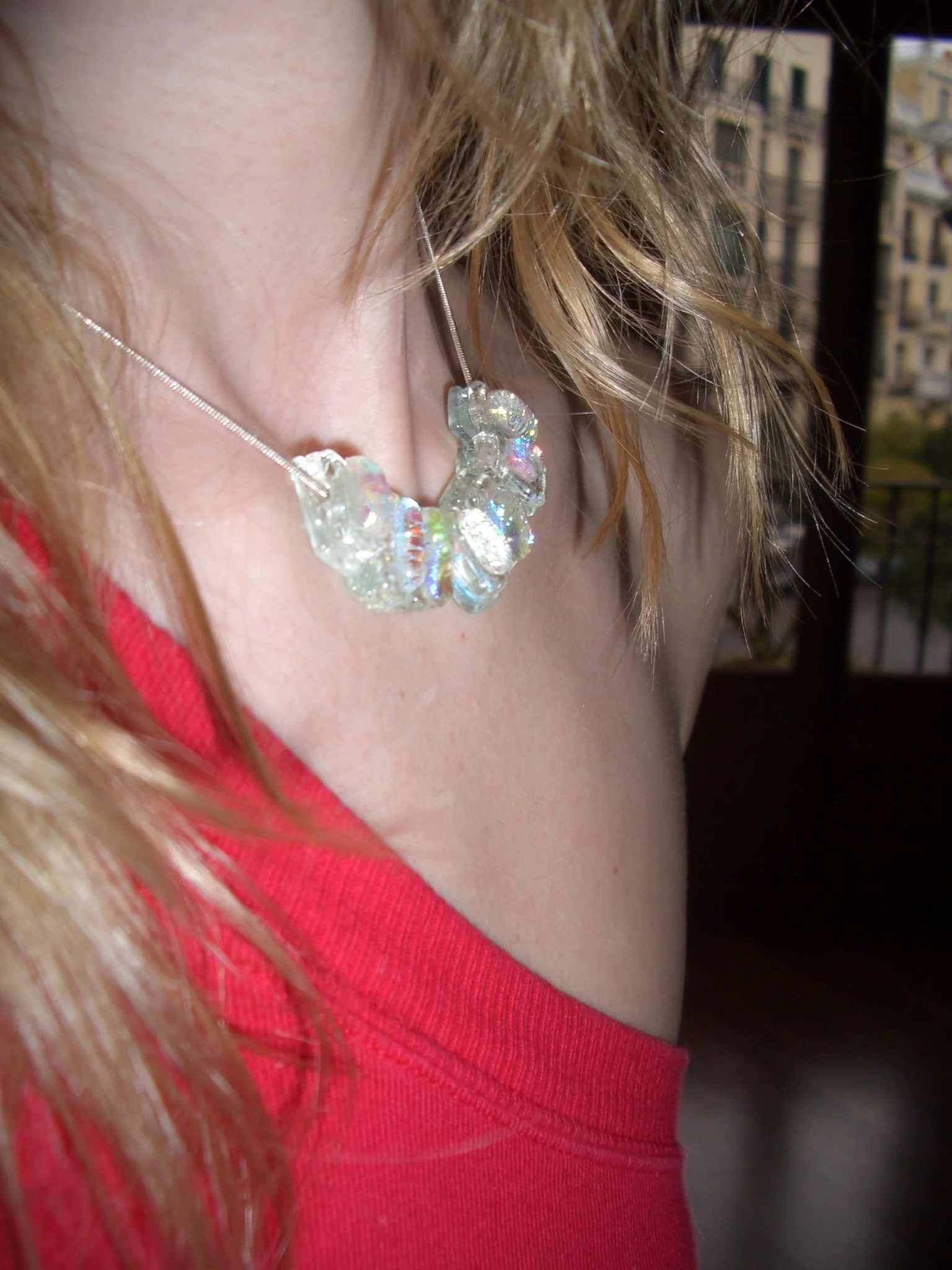 Close-up of a woman's neck and collarbone area wearing a rainbow-colored crystal necklace and a red top.