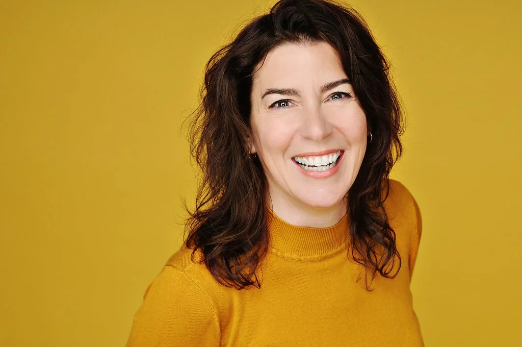 Photo of Hope Lafferty, smiling, shoulder length brown hair, wearing a mustard yellow top.