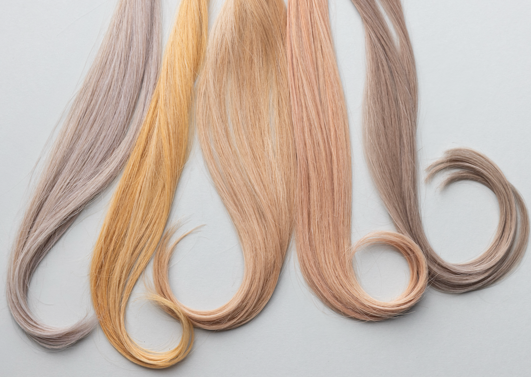 Swatches of various pastel-colored hair extensions in shades of gray, yellow, pink, and brown laid out on a gray background.