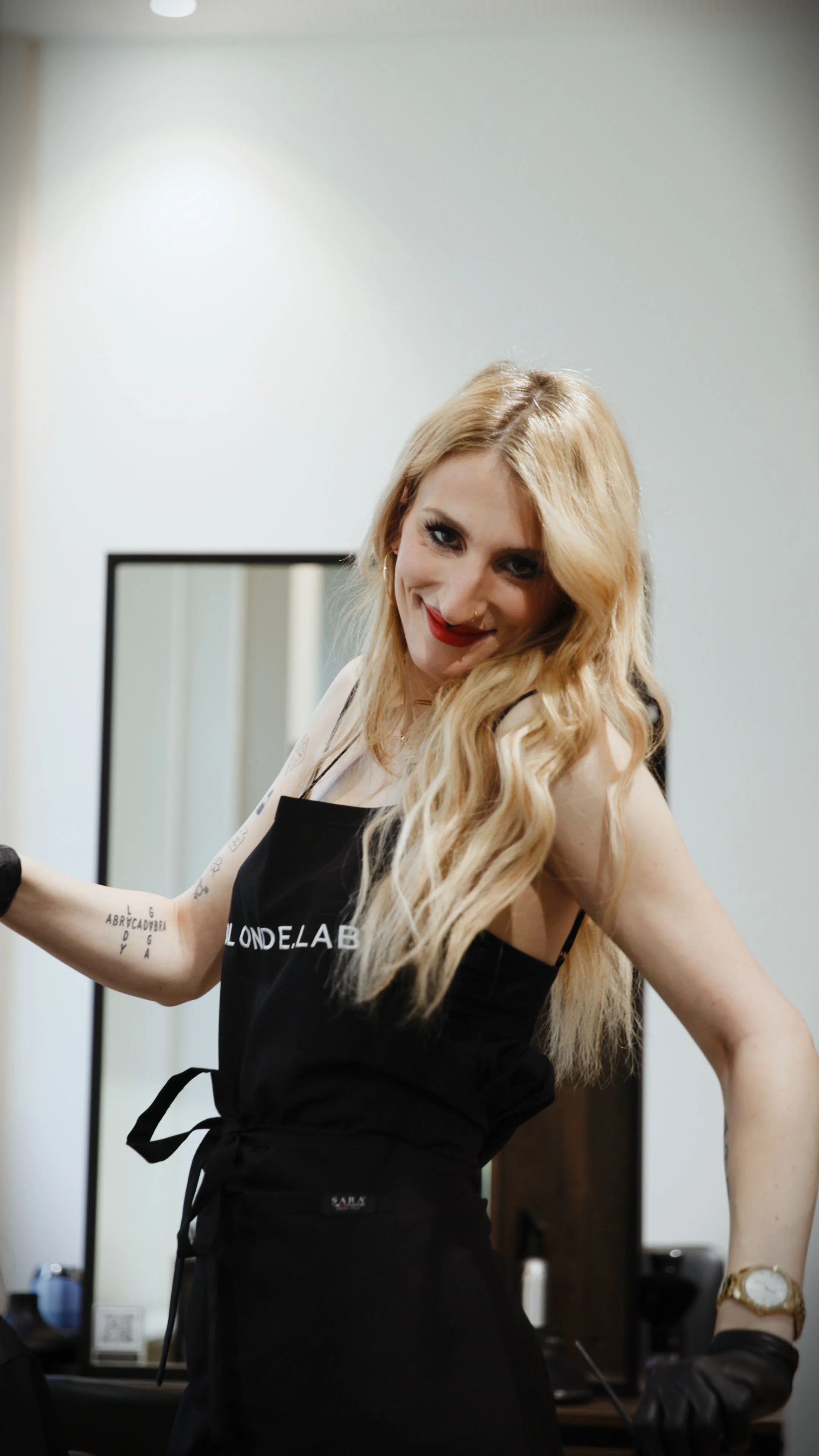 A woman with shoulder-length light brown hair, wearing a black spaghetti strap dress with cutouts, posing against a gray background.