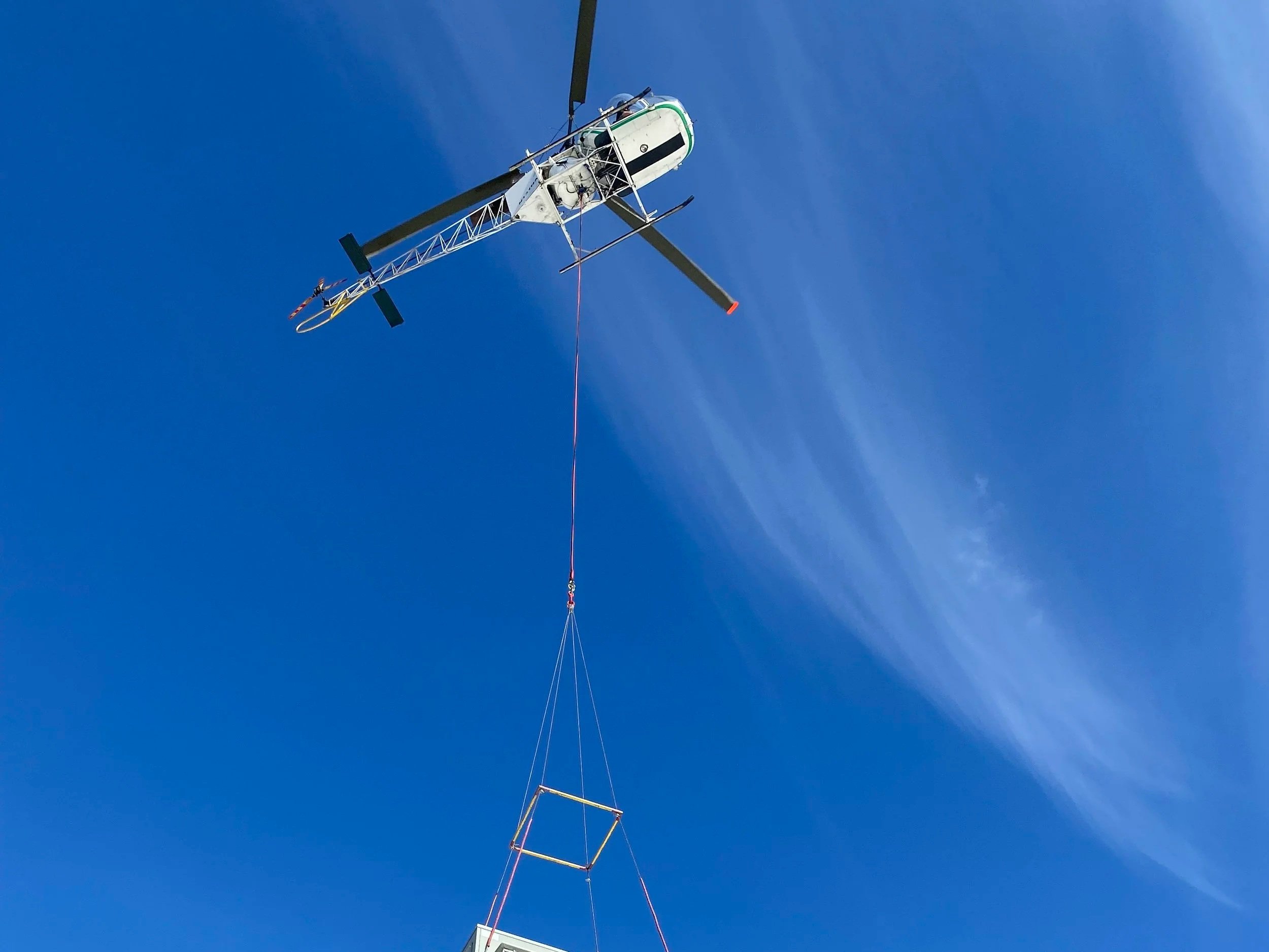 Close-up of a military helicopter with its rotor blades extended, and a tall communication tower in the background against a clear blue sky.