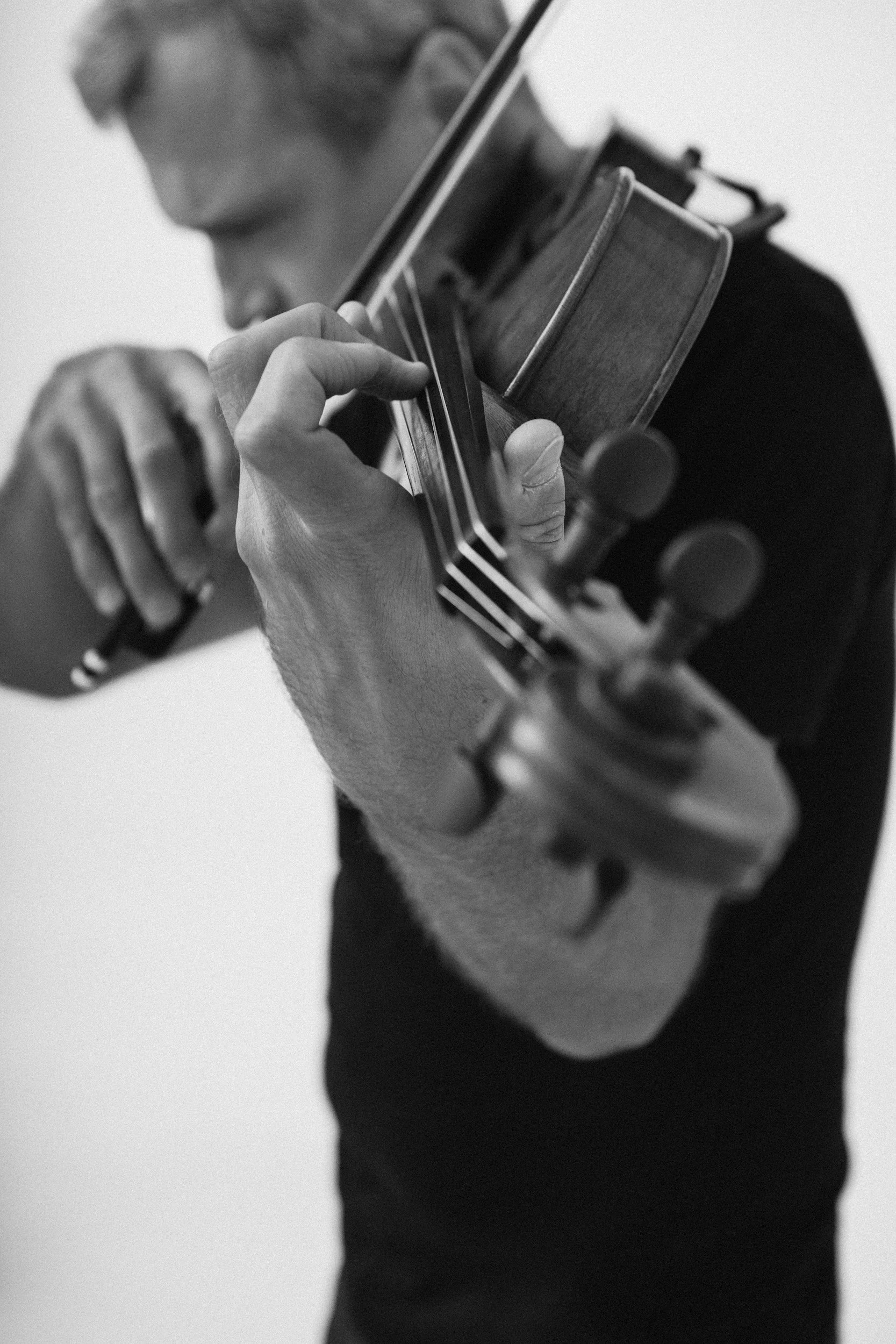 A man playing an acoustic violin, focusing on his hand and the instrument.