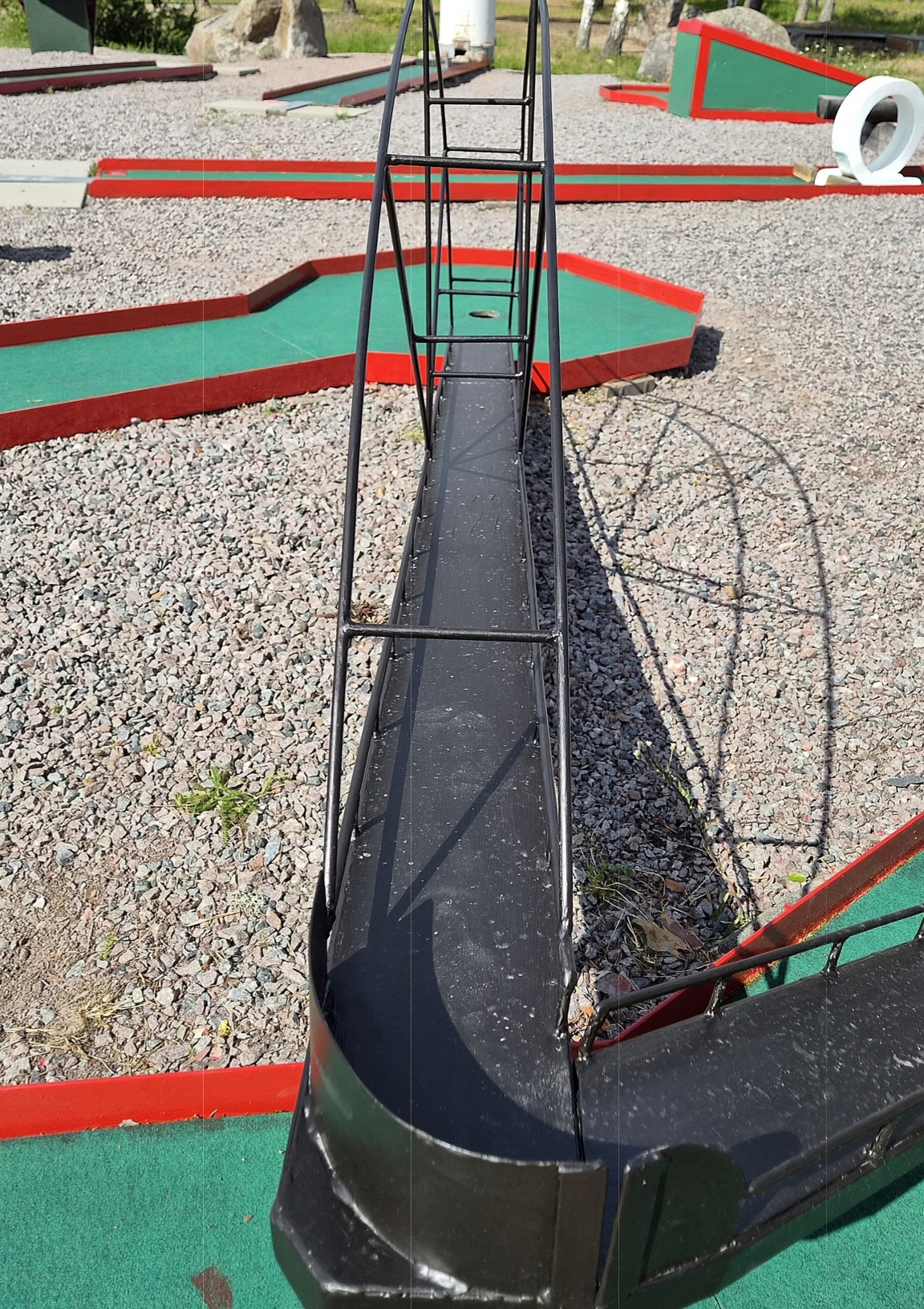 En minigolfbana på Rullsand med en svart bana och ett trädäck, där minigolfhål är markerade med rör och vita cirklar.