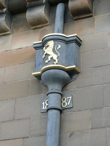 A decorative shield with a gold lion emblem mounted on a building wall, with the numbers 1887 below it.