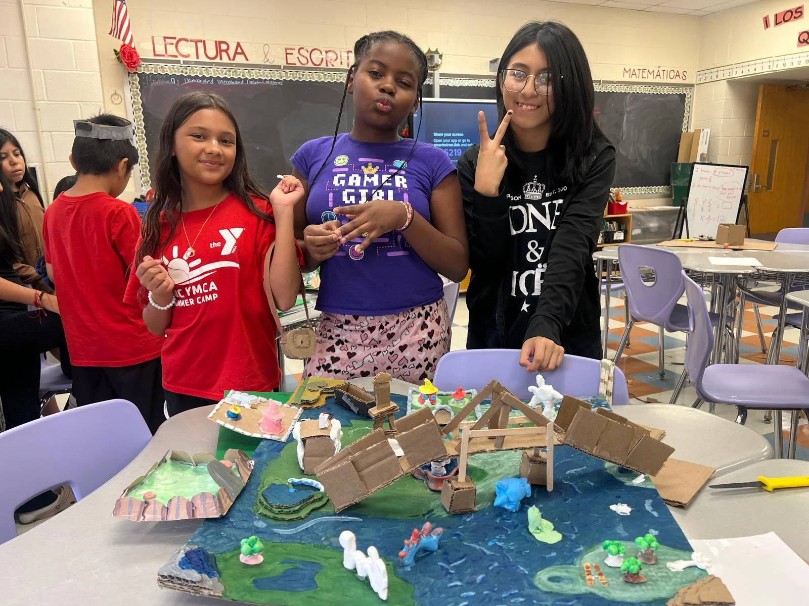 Three girls in a classroom standing over a table with a handmade map on it