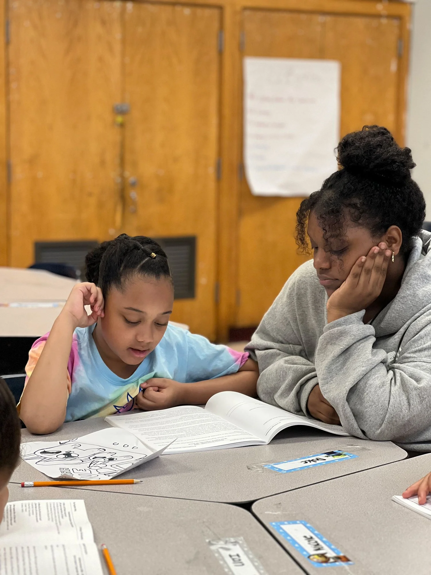 Young girl reading from a workbook while an older mentor watches