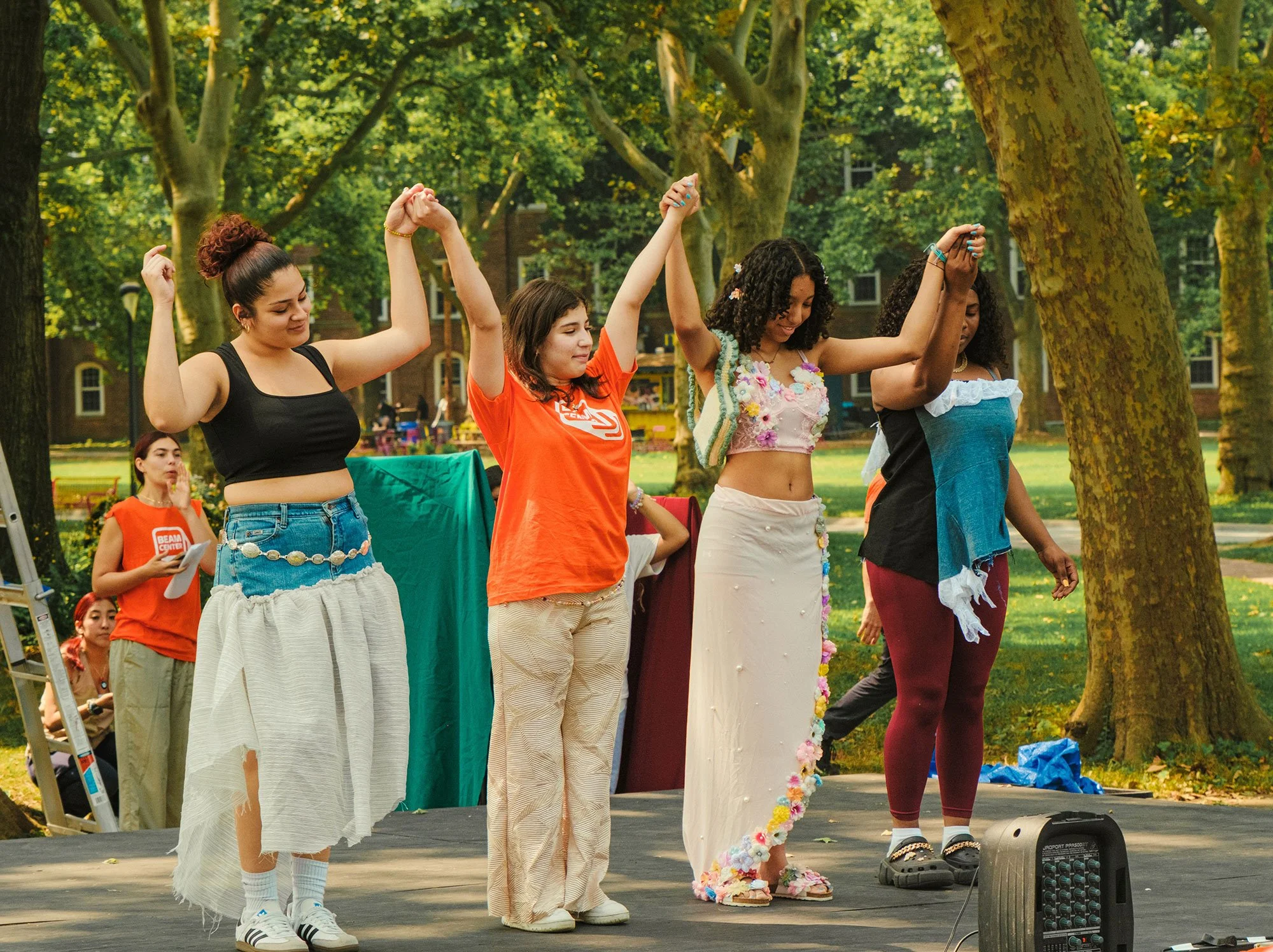 4 students holding each other's hands up in the air while modeling garments at a youth fashion show