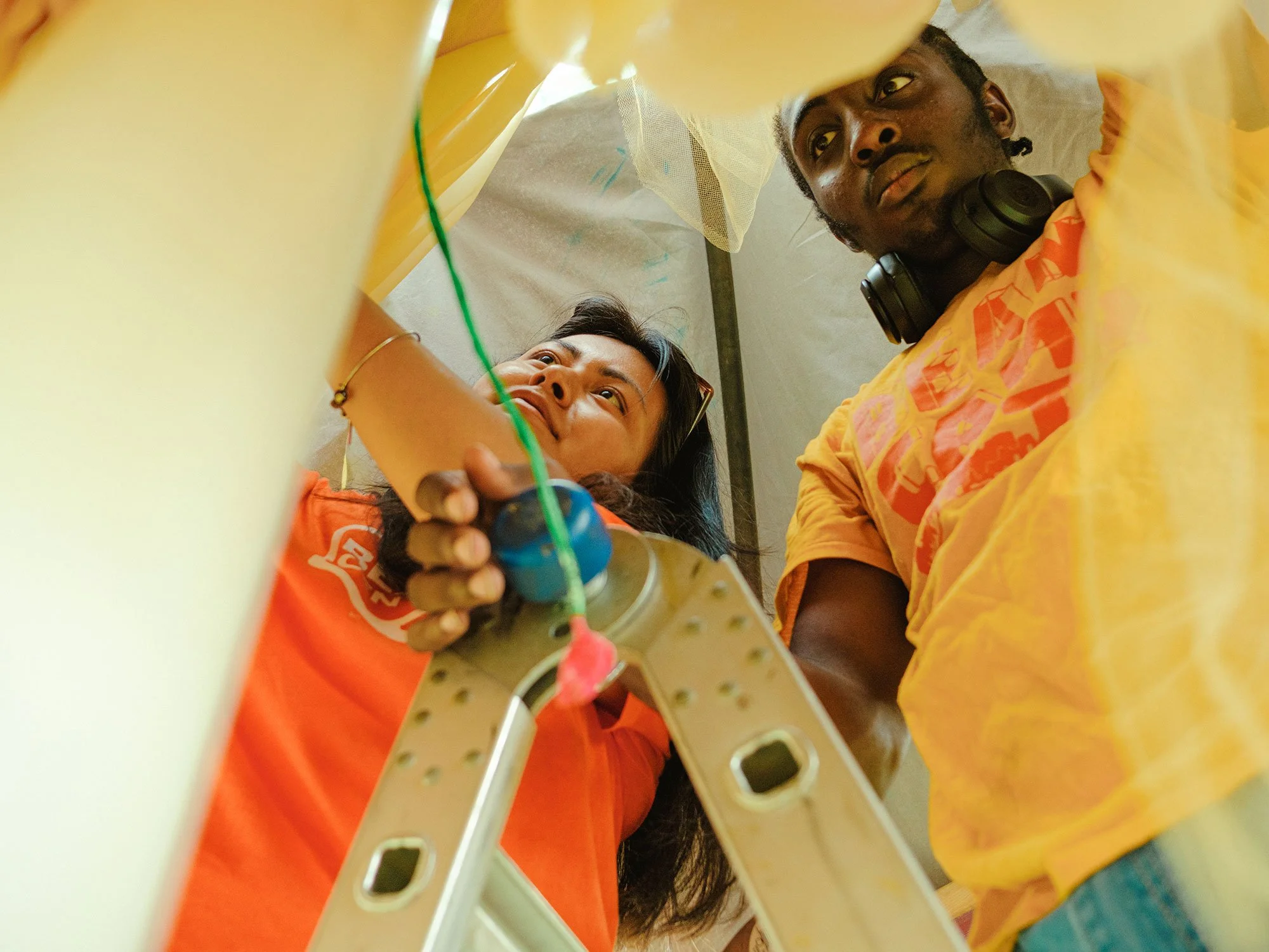 Two Beam students working on a ladder to construct a project for OtherWorlds Fair in 2024.