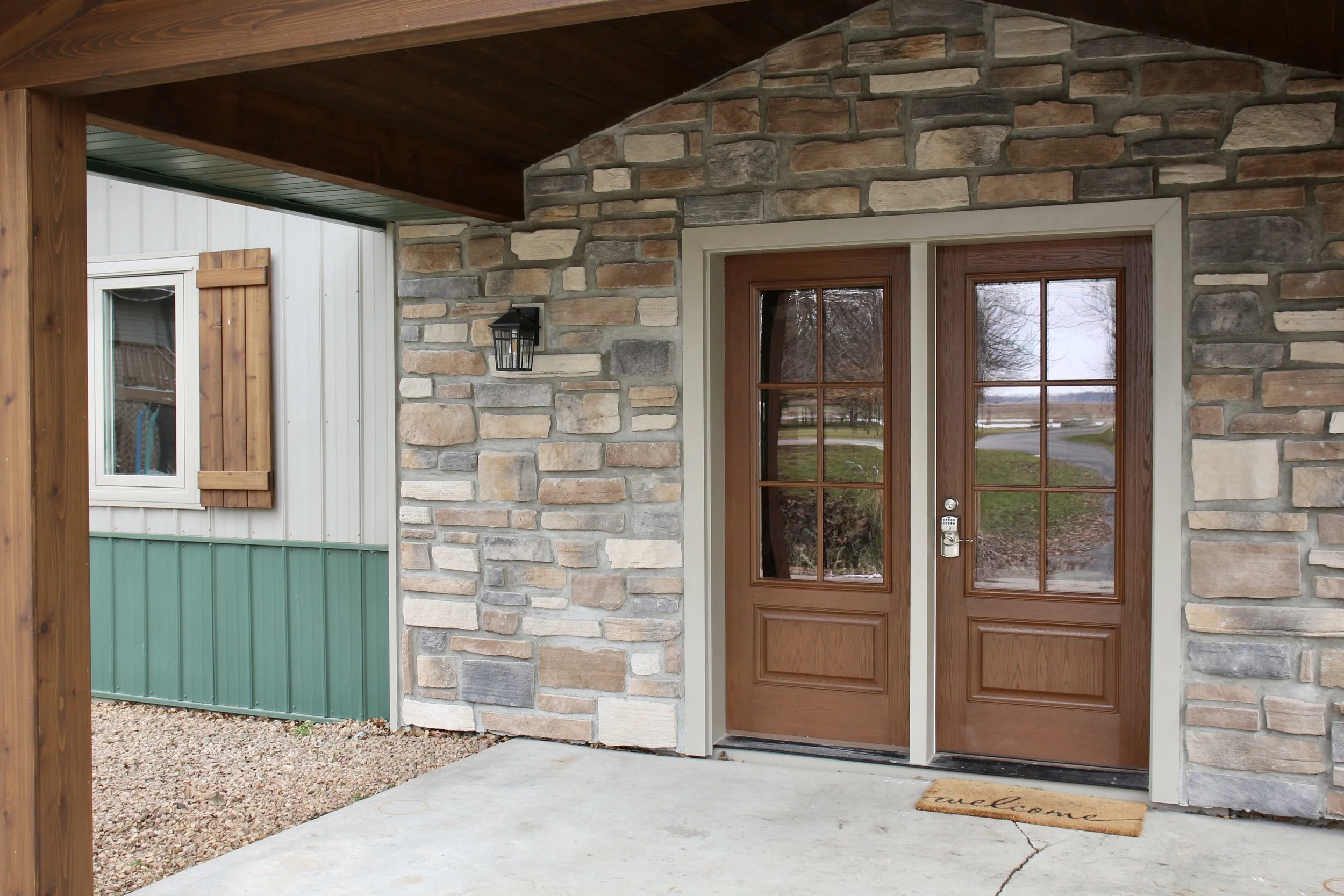 Covered front entrance with a stone facade and 3/4 view wood-look double doors