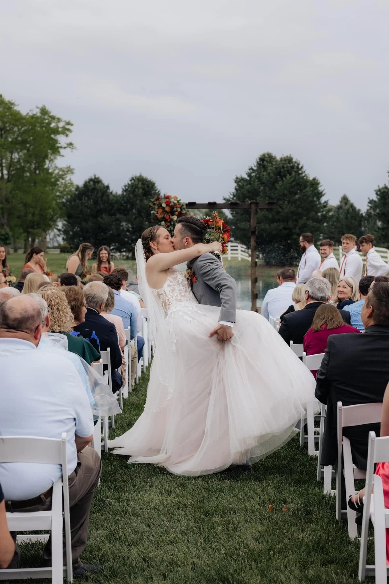 bride-and-groom-kissing-in-aisle-outdoors-lakeside-with-decorated-arch.jpg
