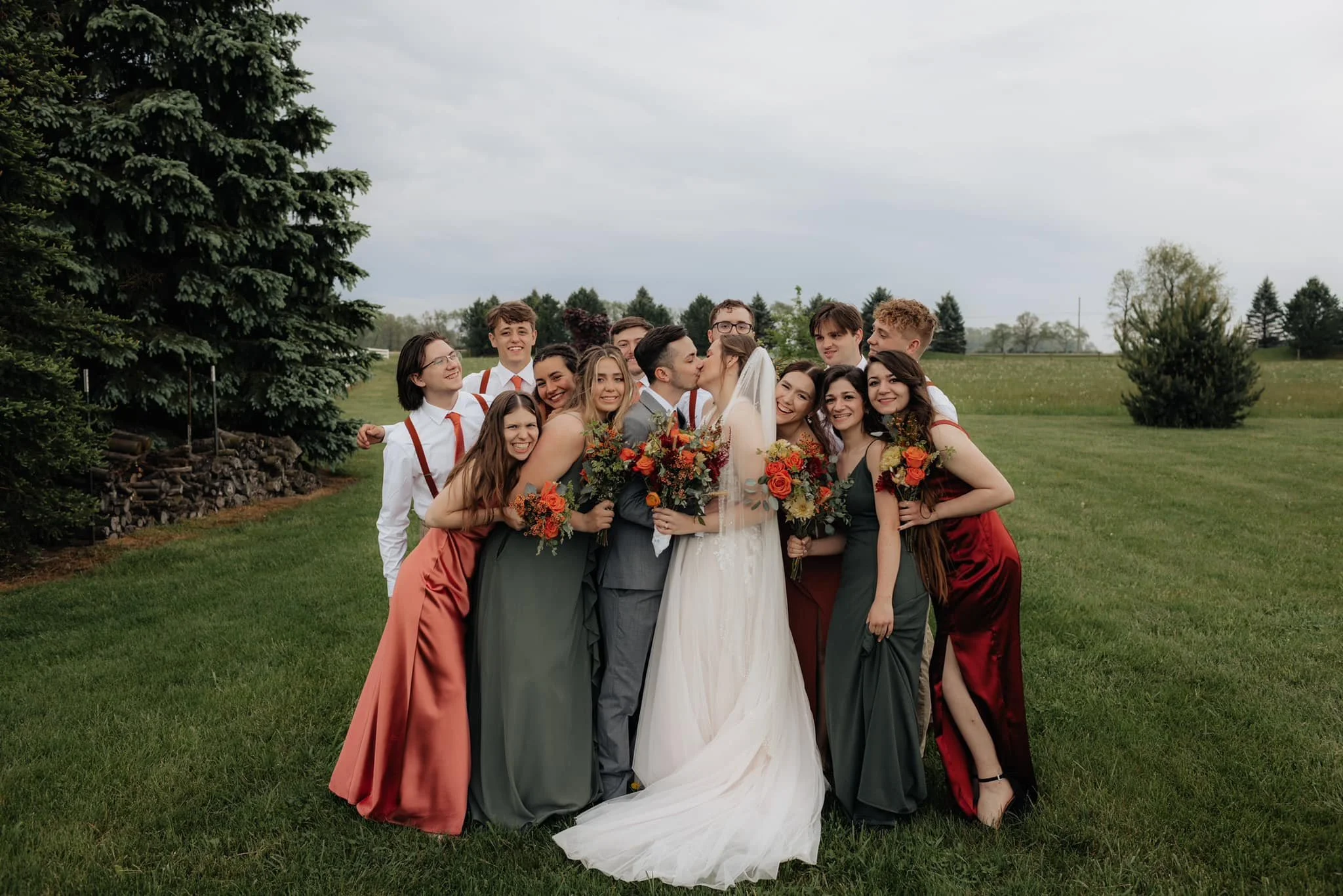 bride-and-groom-kissing-surrounded-by-wedding-party-smiling-outdoors.jpg