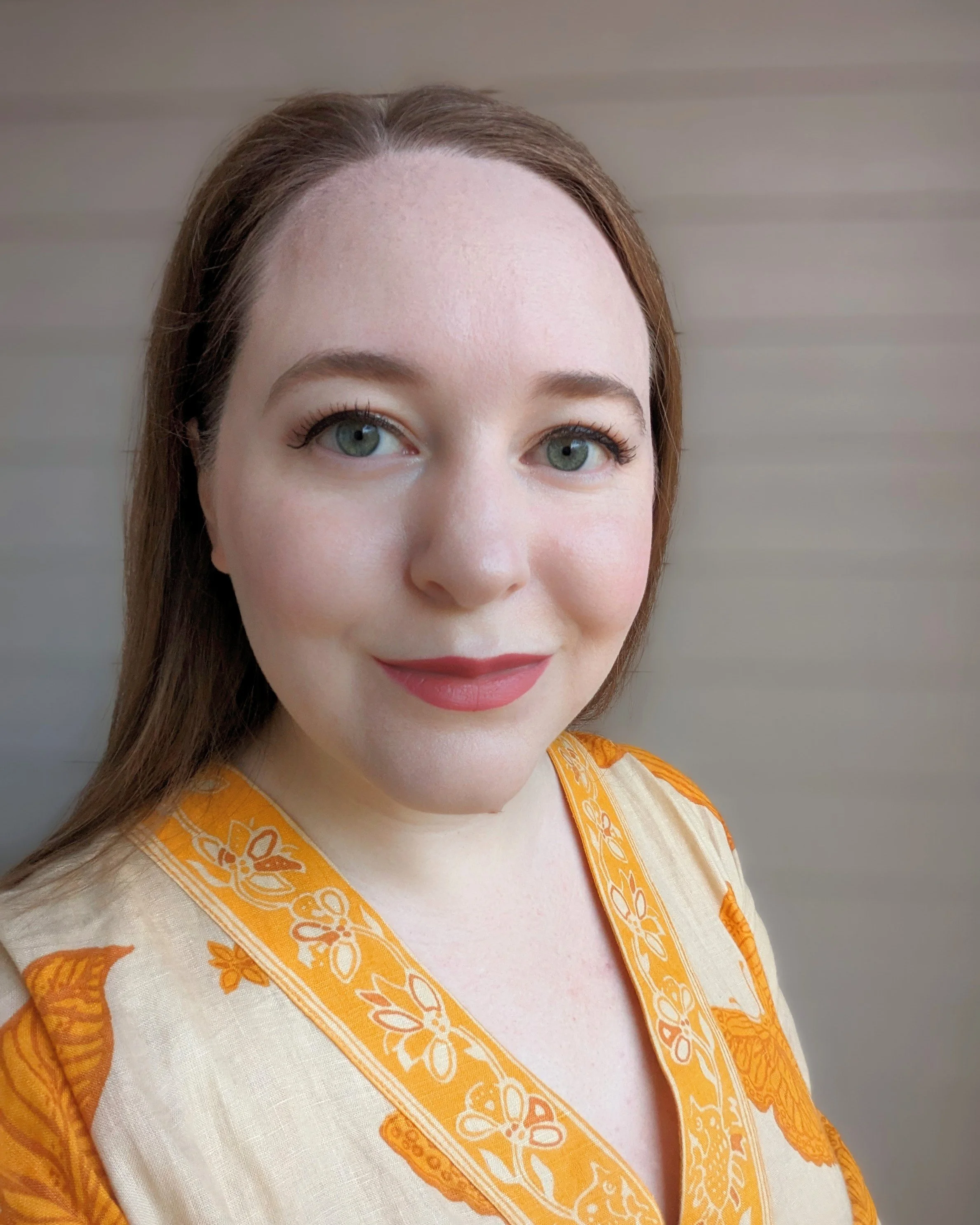 A woman with fair skin, blue eyes, and red hair smiling for a close-up portrait.