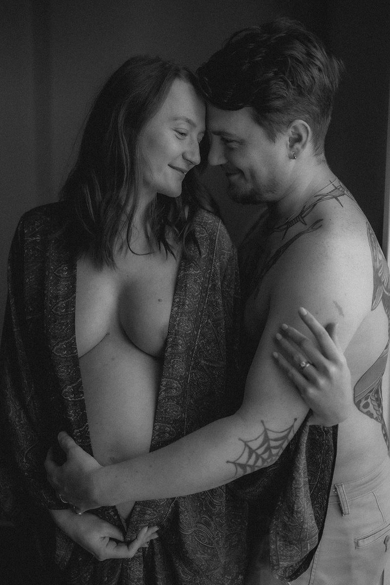 A black and white photo of a man and woman embracing and smiling with their foreheads touching, with the woman partially covered by a patterned cloth.