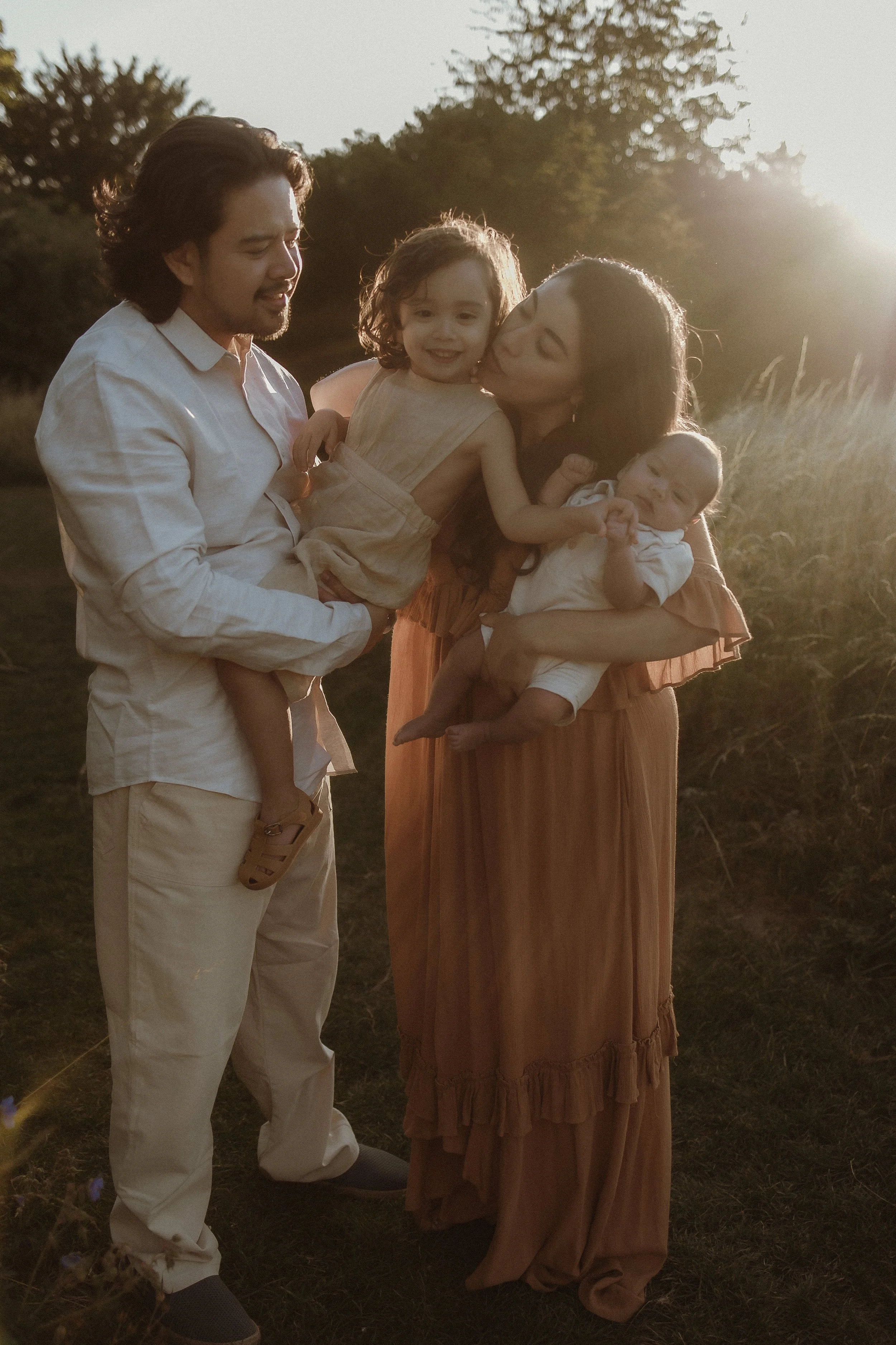 A family of four enjoying outdoor sunset, with mother and father holding a young girl and a baby.