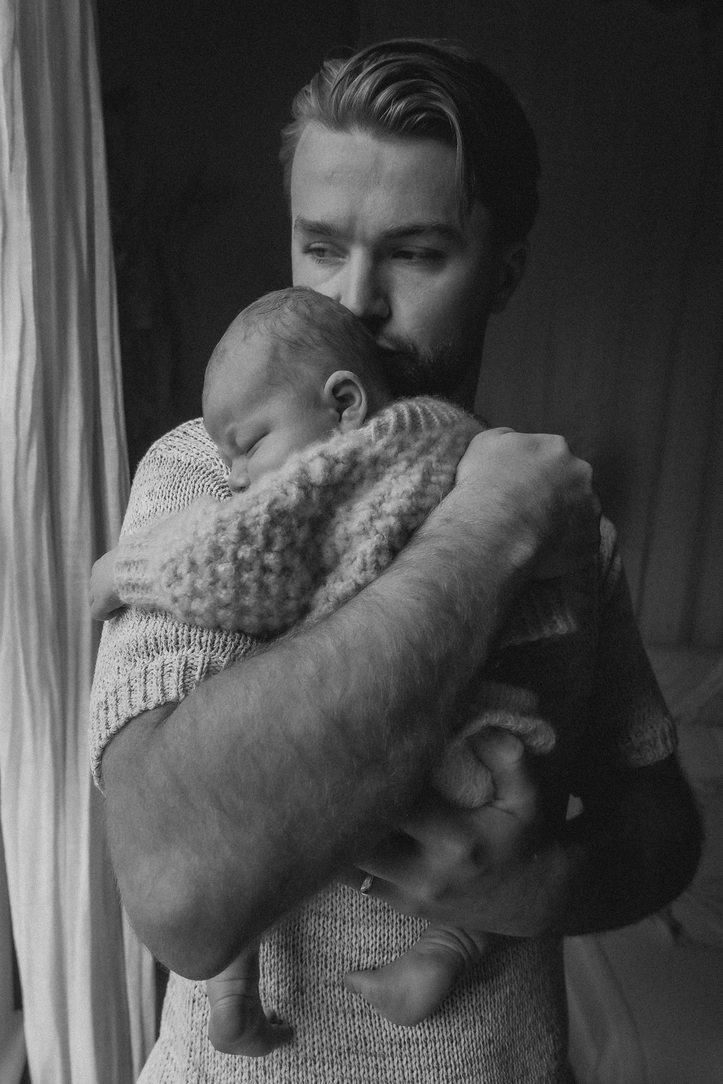 A natural photoshoot of Dad holding his sleeping baby close to his chest in a comforting embrace.