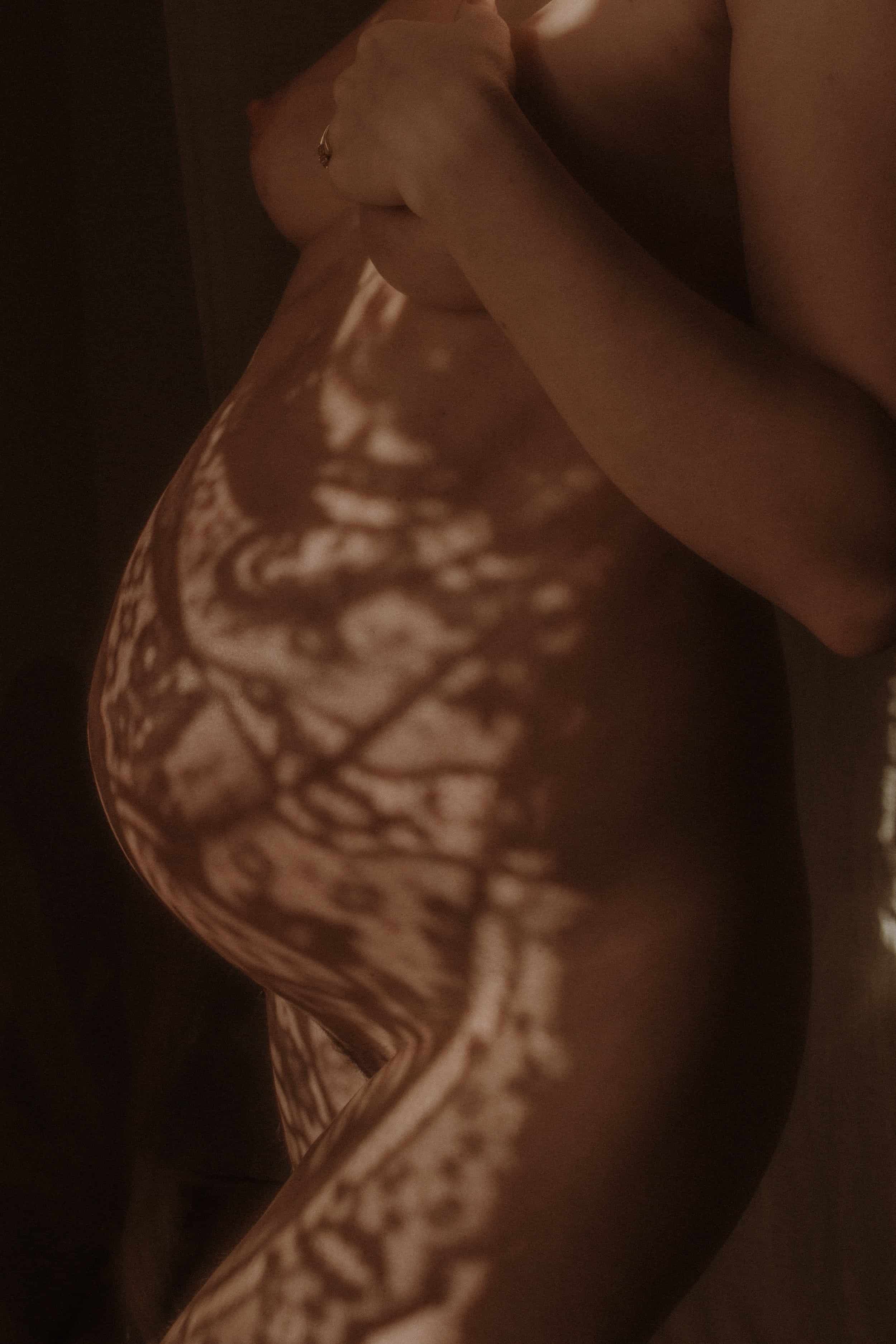 Close-up of a person's body with intricate lace-like shadow patterns cast on the skin, in a dimly lit setting.