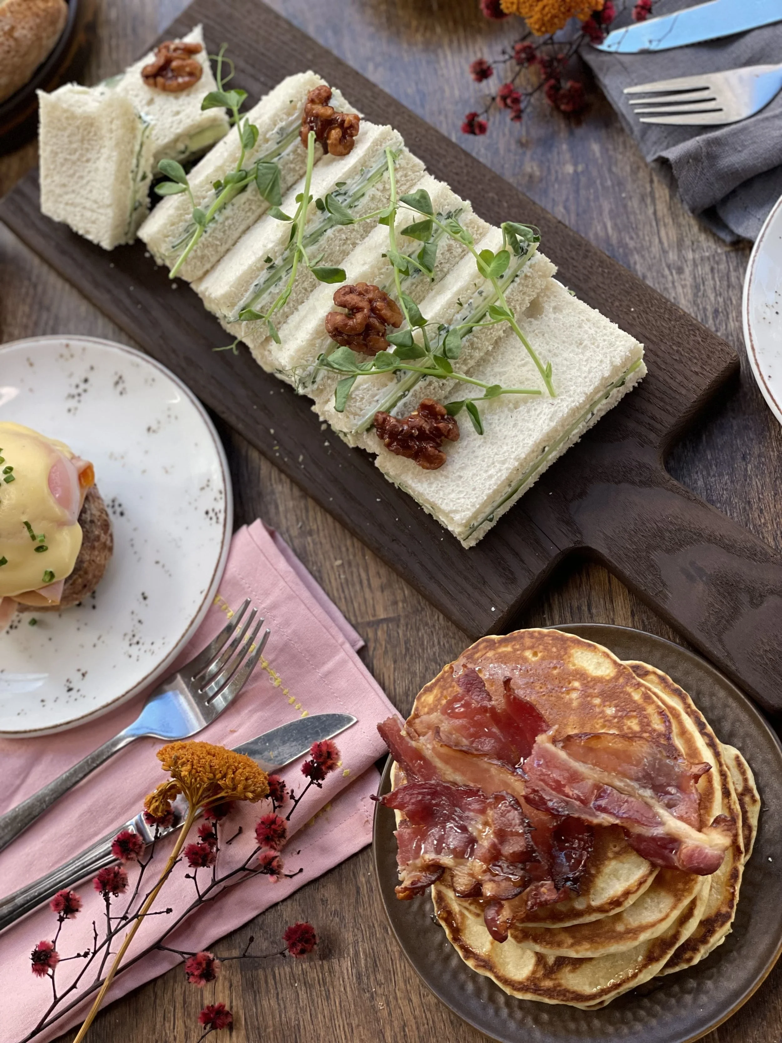 Nærbildet av lunsjretter på et bord. Pannekaker med bacon, eggs benedict, rekke med sandwicher dandert med urter og valnøtter