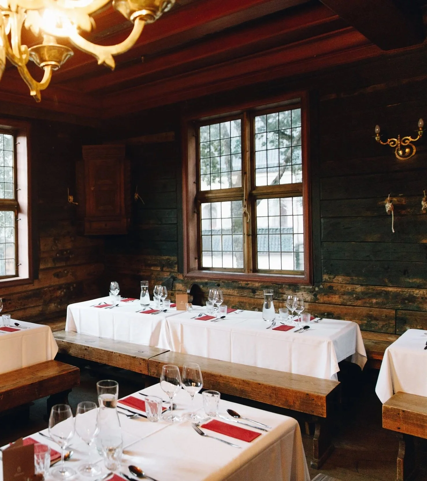 Julebord dekket for selskap i Schøtstuene, med hvite duker og lysekroner i tømmerstuen.