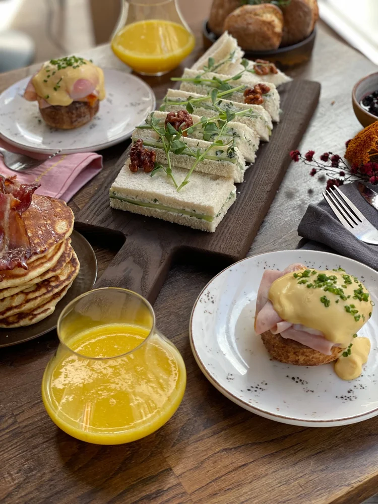 Poached eggs with hollandaise sauce and ham, small sandwiches with walnuts, and freshly baked scones on the brunch table at Allmuen Bistro