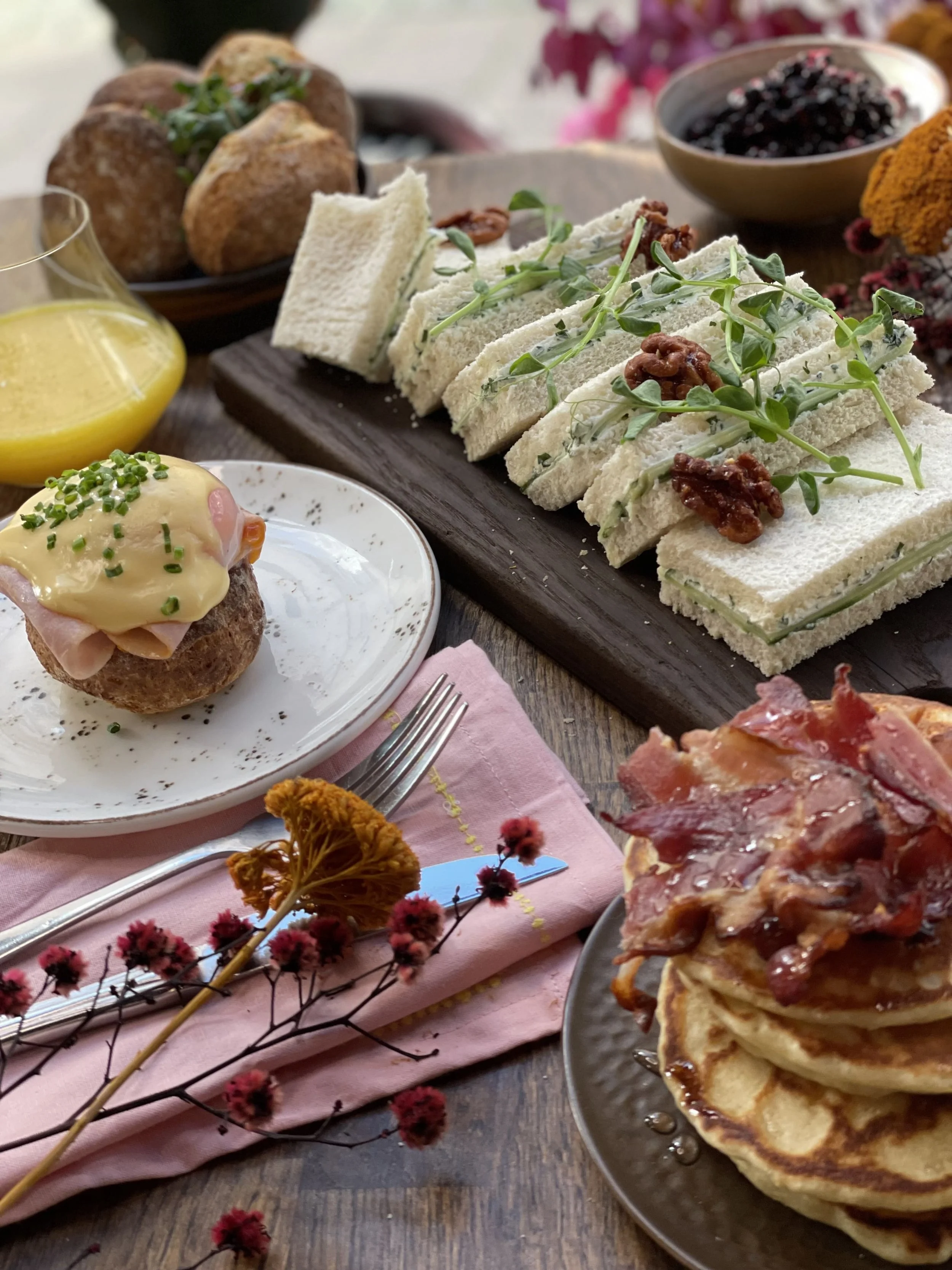 Sidebildet av lunsjretter på et bord. Pannekaker med bacon, eggs benedict, rekke med sandwicher dandert med urter og valnøtter, juice og rundstykker