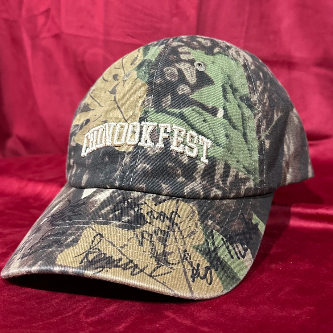 Detailed close-up of CHINOOK FEST embroidered camo hat with visible signatures from all Hippies & Cowboys band members on the brim.