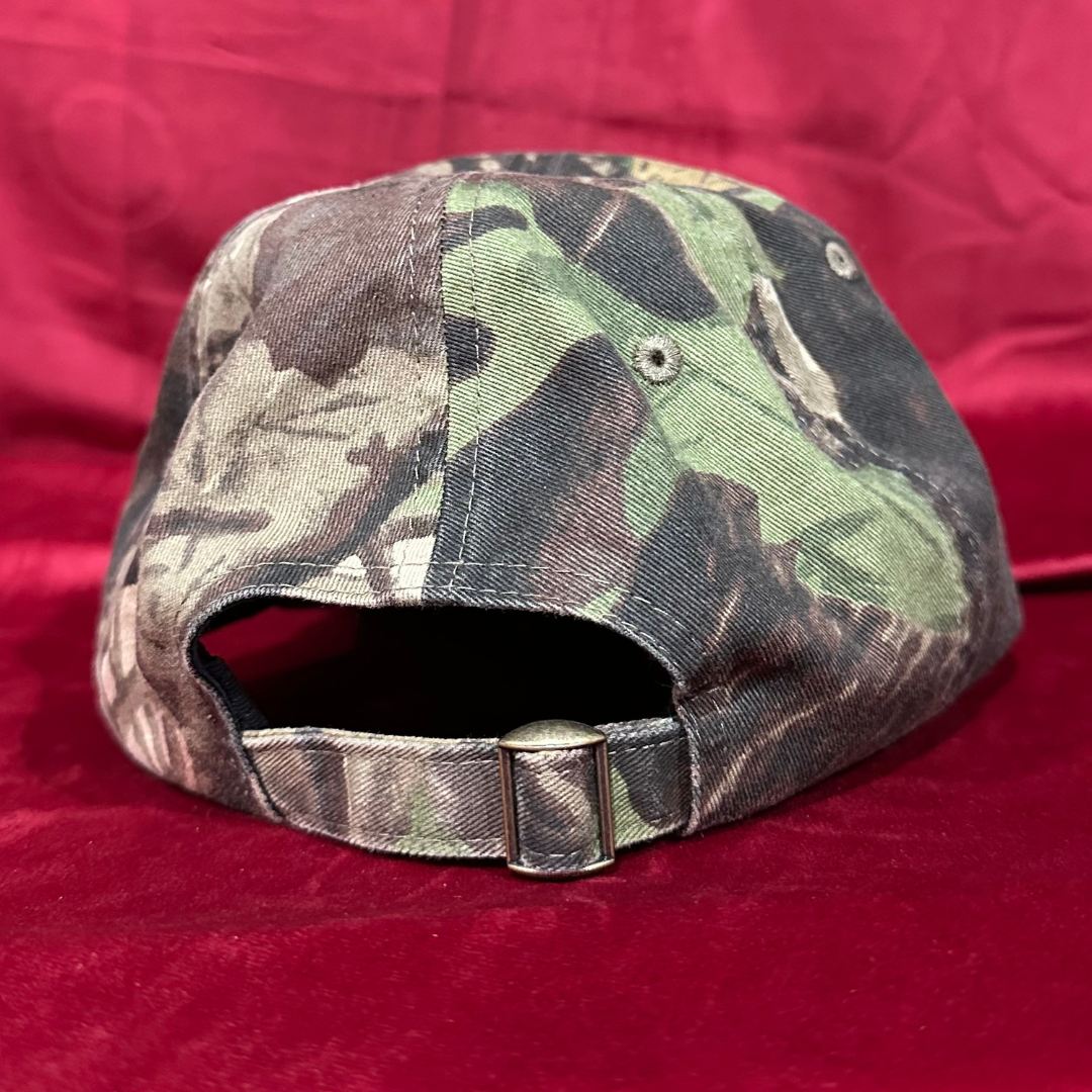 Rear view of Hippies & Cowboys signed Chinook Fest camo hat featuring adjustable fabric strap and metal slide buckle, shown against red background.