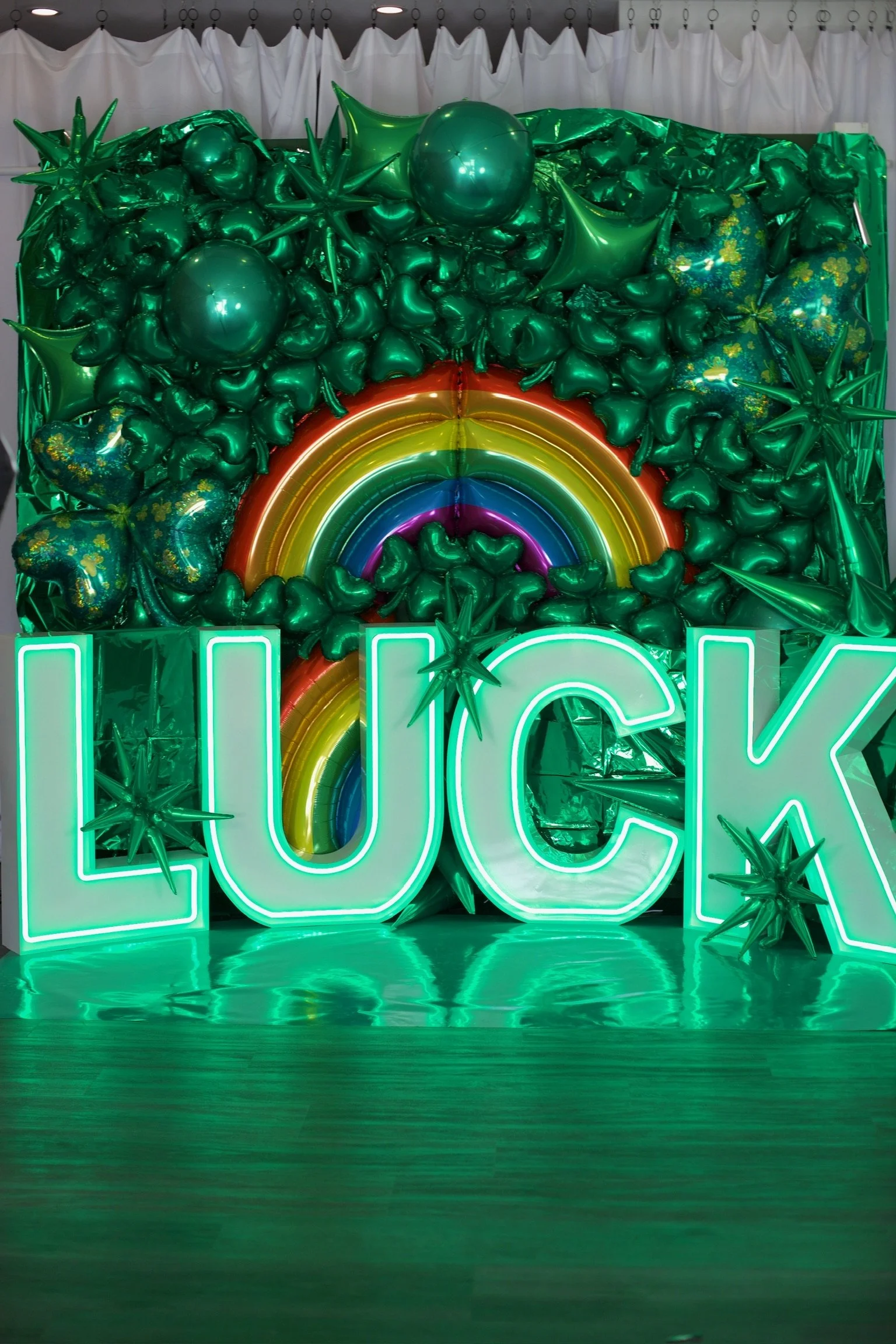 Colorful balloon display with a rainbow and the neon word "LUCK" in front.