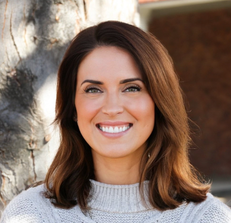 A woman with shoulder-length brown hair and fair skin smiling outdoors with a tree trunk in the background.