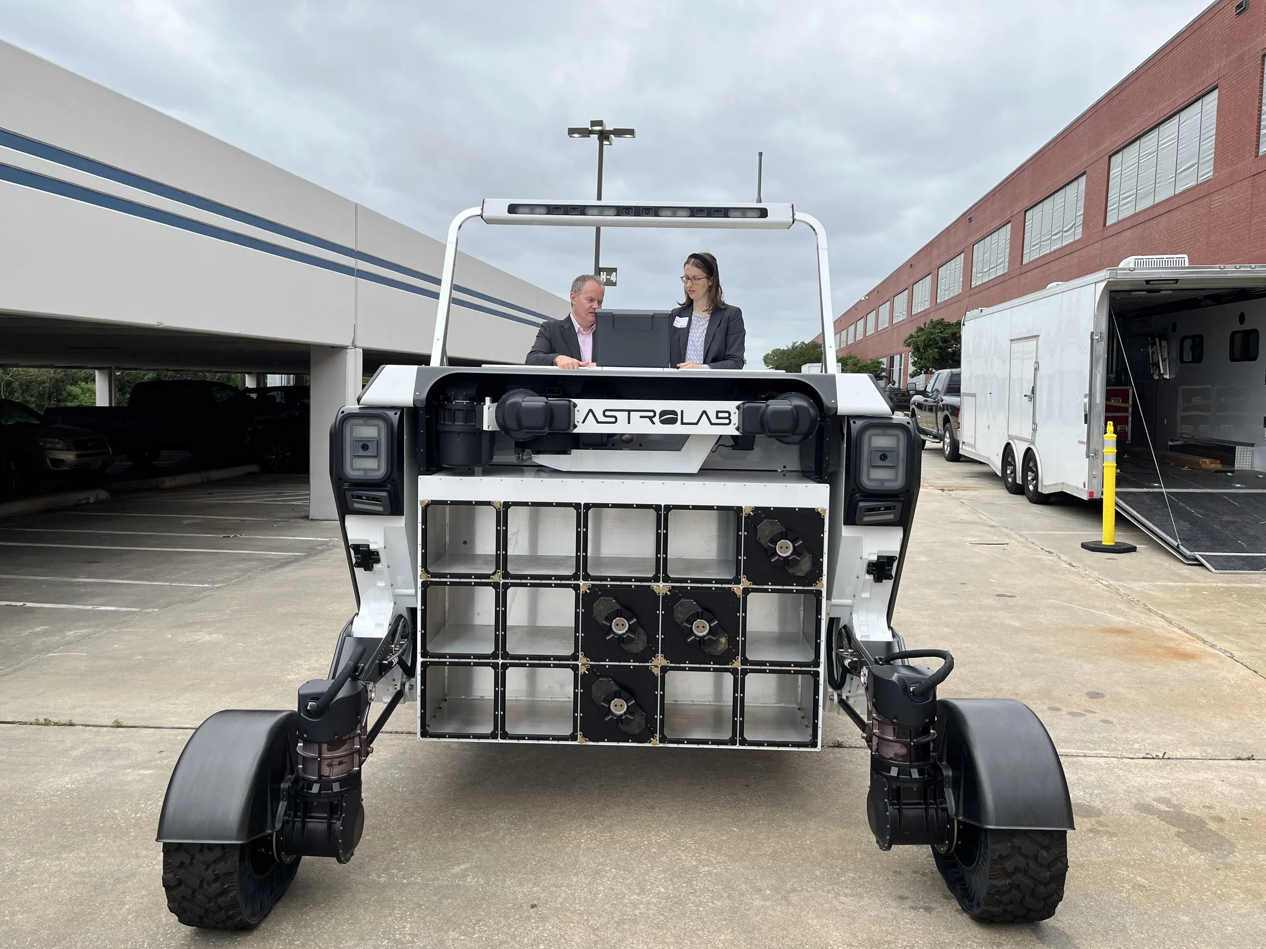 A large robotic vehicle labeled "AstroLab" is outdoors, with Erin and the CEO of the rover company driving it