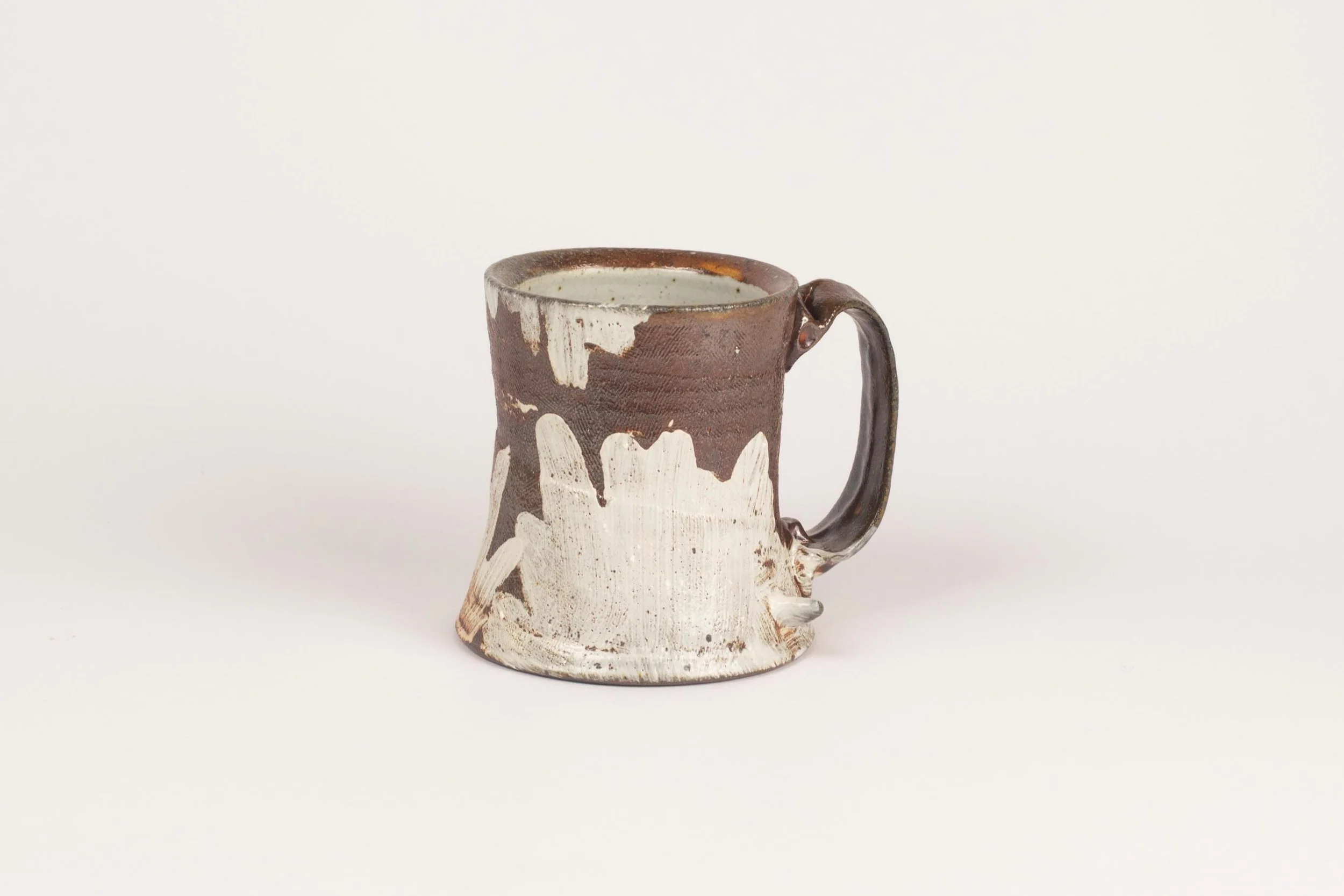 I love the contrast of the dark clay body and roughly brushed white slip on this cup. It allows the movement of the decoration to breathe and be seen. As a painter, there is something so emotional about an expressive brush stroke and I&rsquo;m please
